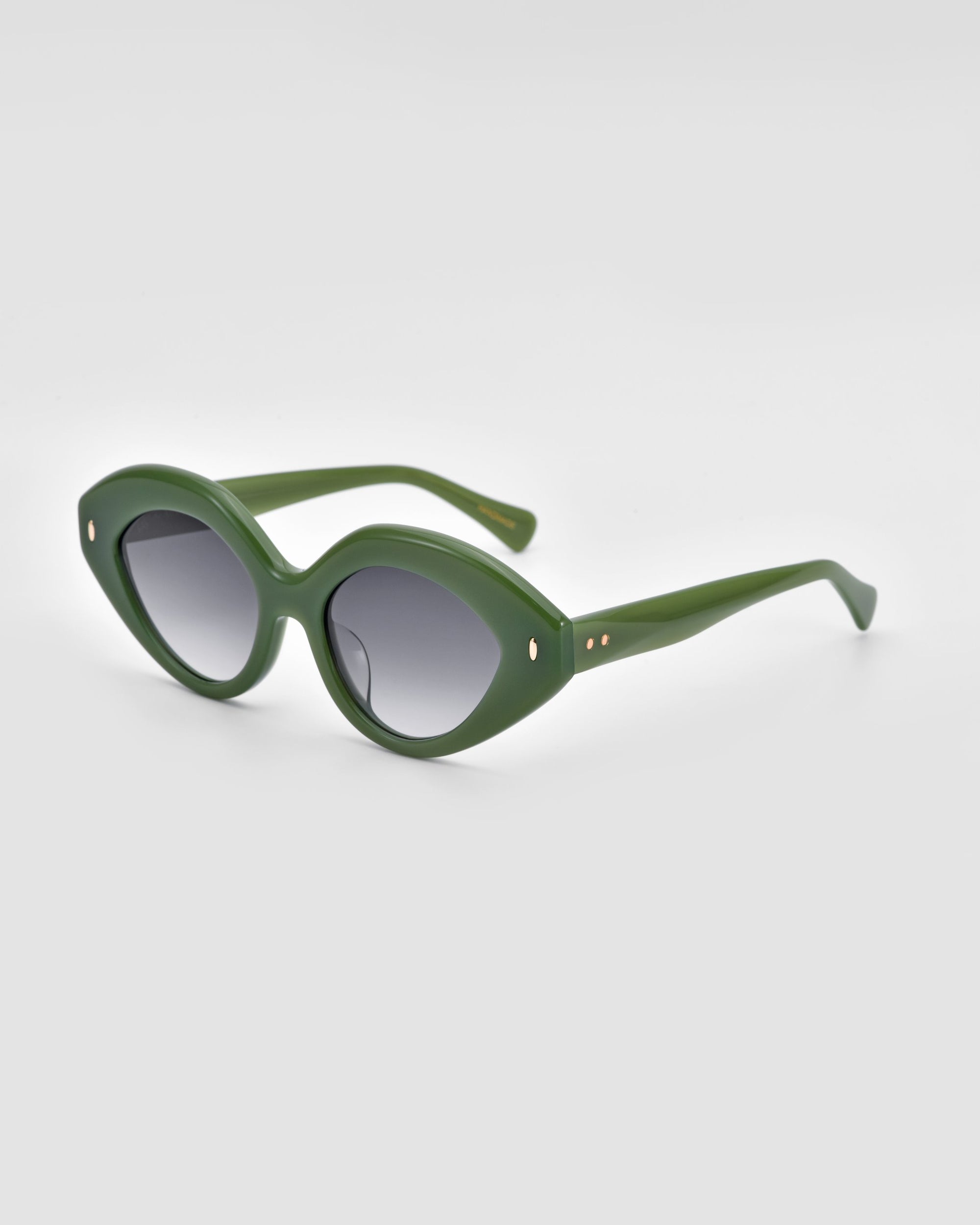 Introducing Vera by For Art&#39;s Sake®: stylish and eco-friendly green-framed sunglasses with dark tinted lenses. The frames feature a slightly rounded, oval shape, adorned with small decorative gold dots on the temples near the hinges, all set against a plain, light-colored background.