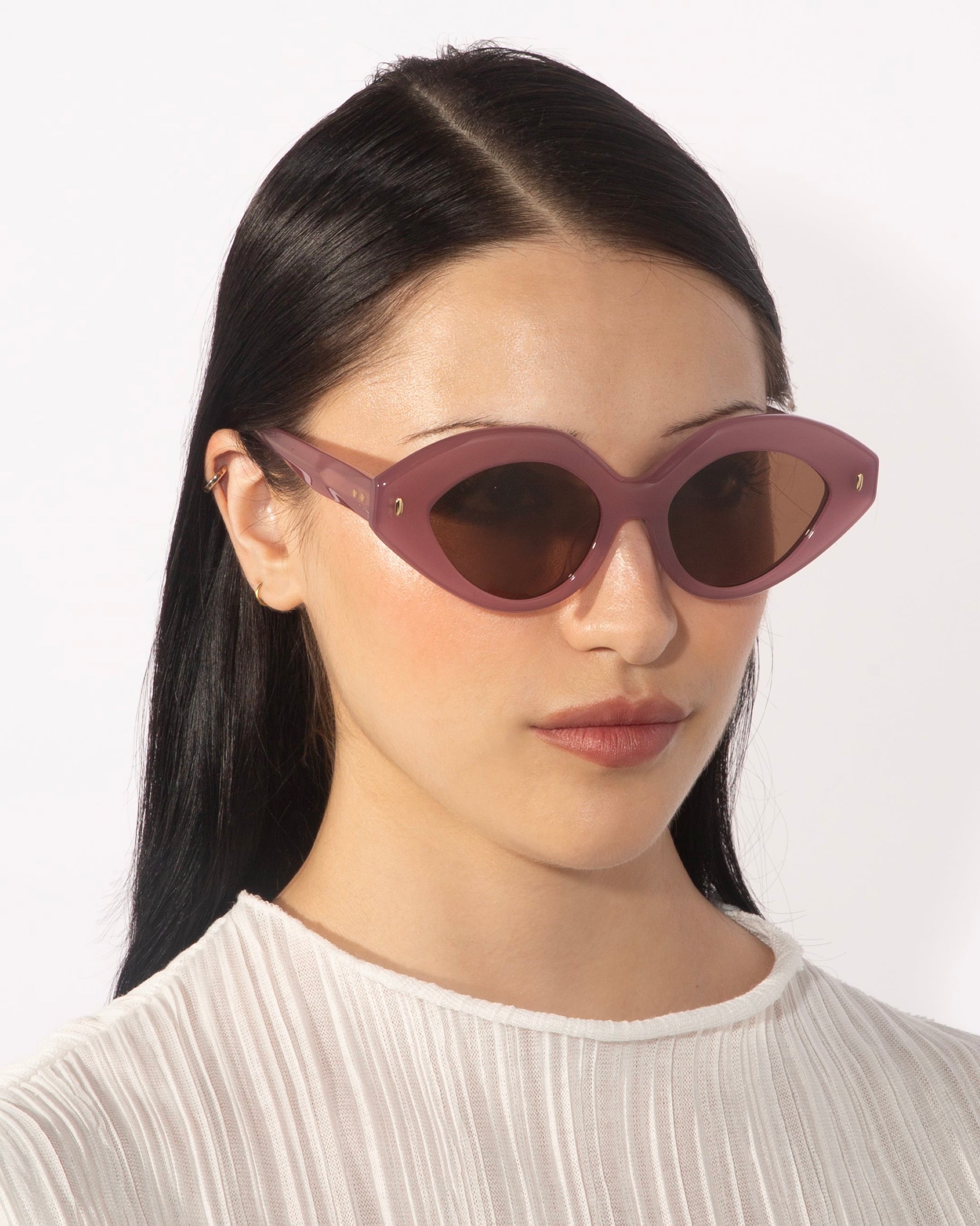 A person with long, straight, dark hair is wearing a white pleated blouse and oversized Vera sunglasses, designed with faceted acetate by For Art&#39;s Sake®. The background is plain white.