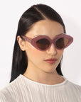 A person with long, straight, dark hair is wearing a white pleated blouse and oversized Vera sunglasses, designed with faceted acetate by For Art's Sake®. The background is plain white.