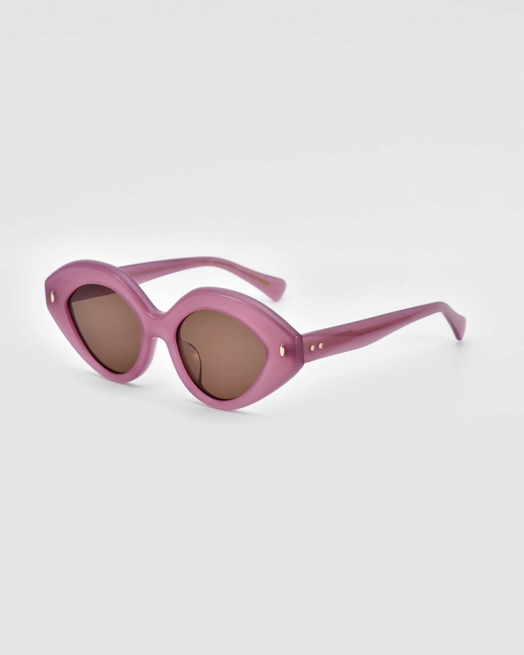 The Vera sunglasses by For Art&#39;s Sake® are showcased against a plain white background, featuring an oval-shaped, cat-eye design with a pink frame and brown-tinted lenses. The pink temples are embellished with small gold accents near the hinges, highlighting their unique blend of style and eco-friendly materials.