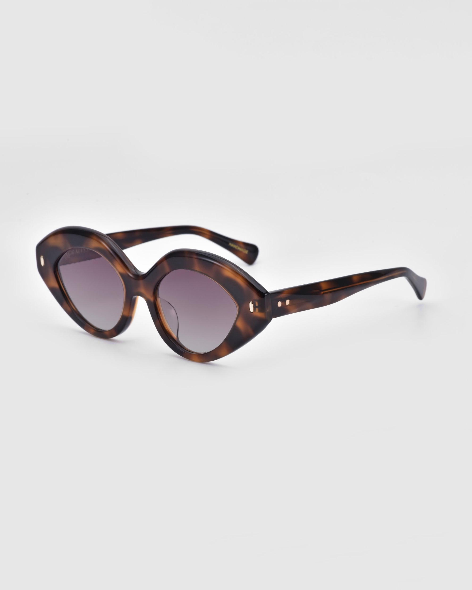 The Vera sunglasses by For Art&#39;s Sake® are positioned against a plain white background. These eco-friendly, tortoiseshell oval sunglasses feature dark lenses and a distinct, slightly curved frame design with a glossy finish and small metal accents on the front near the hinges.