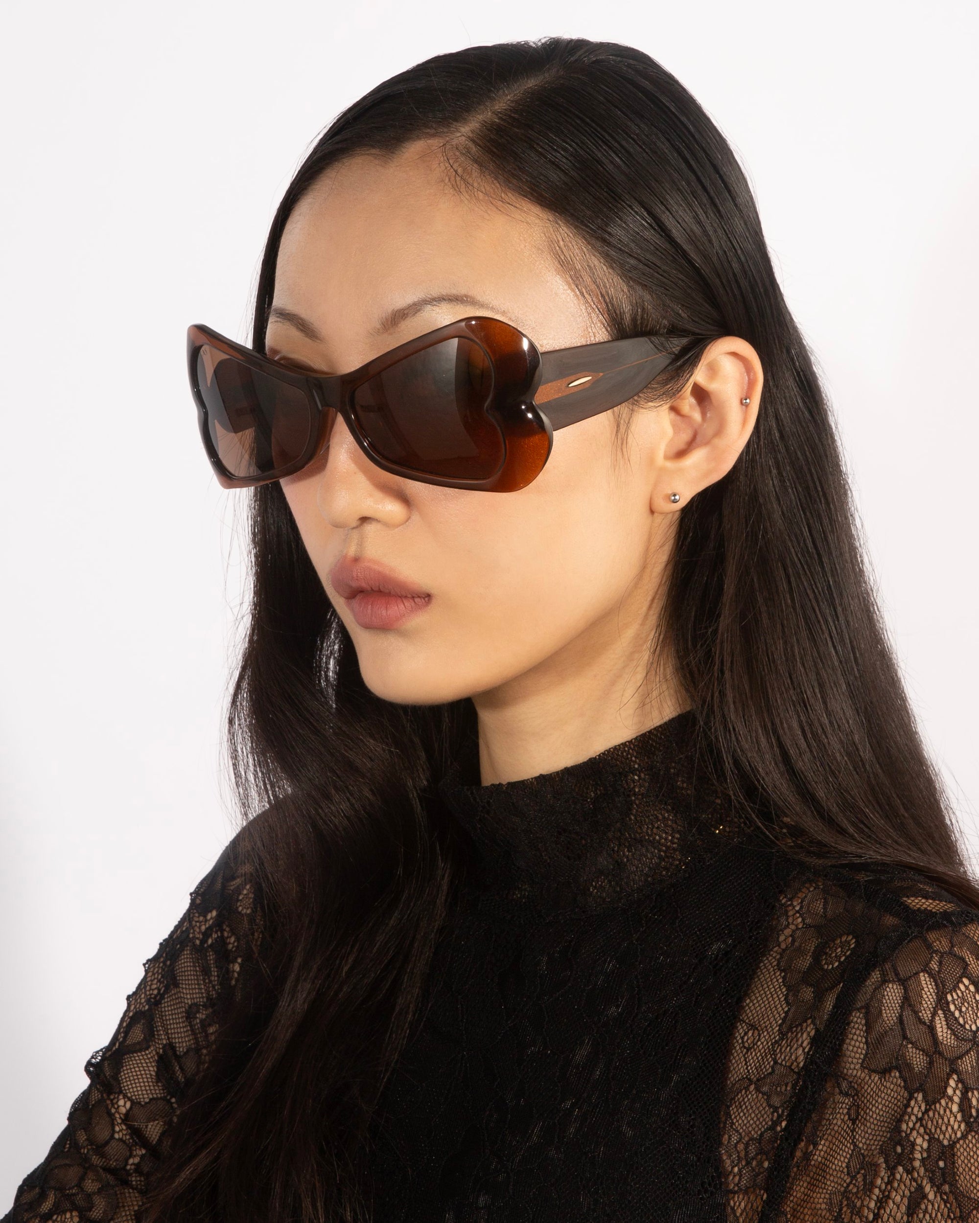 A person with long dark hair is wearing sleek black acetate sunglasses named Bubblegum by For Art&#39;s Sake®, paired with a stylish black lace top, set against a plain white background.