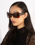 A person with long dark hair is wearing sleek black acetate sunglasses named Bubblegum by For Art's Sake®, paired with a stylish black lace top, set against a plain white background.