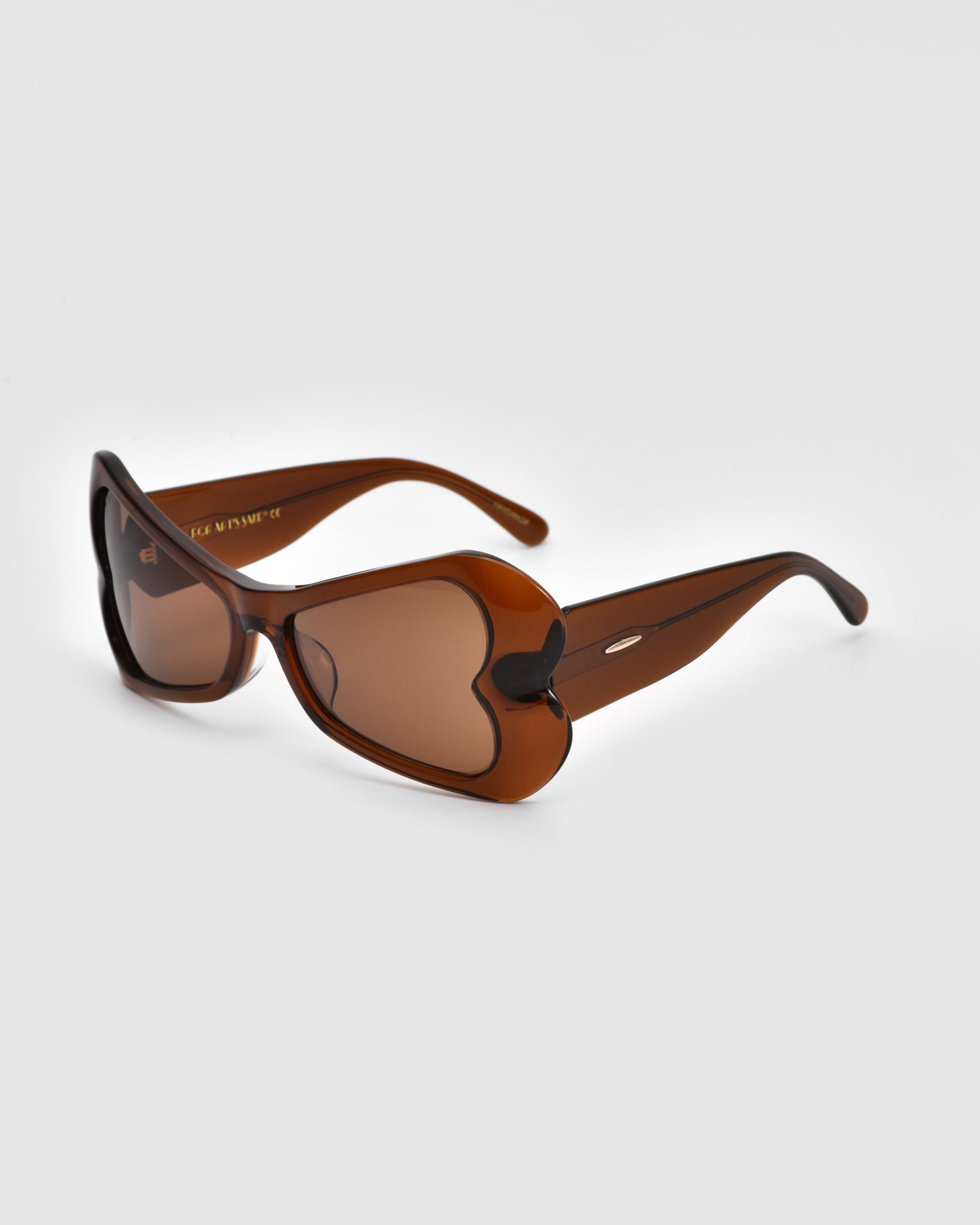 A pair of stylish brown sunglasses from For Art&#39;s Sake®, known as the Bubblegum, featuring heart-shaped lenses and matching brown frames. The bold design is positioned at an angle, showcasing its unique shape and glossy finish, set against a plain white background.