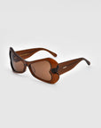 A pair of stylish brown sunglasses from For Art's Sake®, known as the Bubblegum, featuring heart-shaped lenses and matching brown frames. The bold design is positioned at an angle, showcasing its unique shape and glossy finish, set against a plain white background.