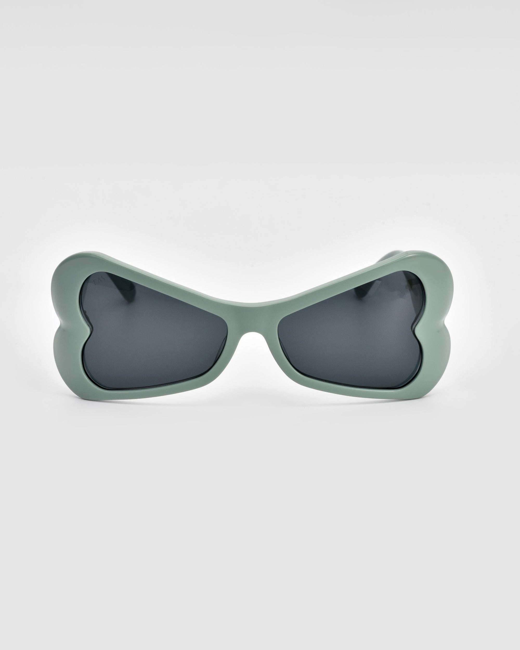 A pair of For Art's Sake® Bubblegum sunglasses features heart-shaped frames in a pale green hue with dark lenses, expertly crafted from sustainable materials, showcased against a plain white background.