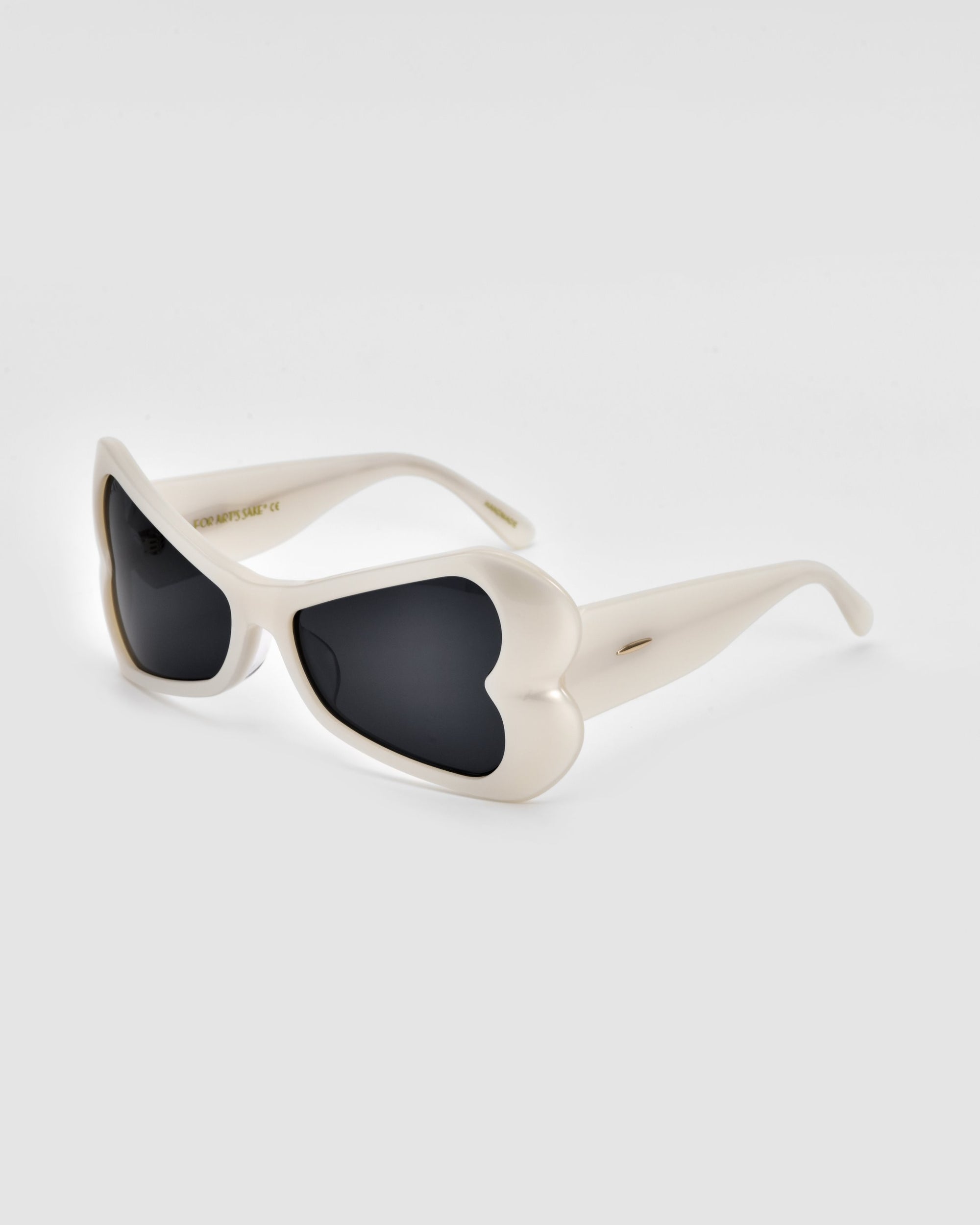 A pair of stylish For Art&#39;s Sake® Bubblegum sunglasses features white frames with heart-shaped lenses tinted in dark black. This bold design is both playful and chic, creating a striking fashion statement. Made from sustainable materials, the sunglasses are positioned against a neutral, light-colored background.