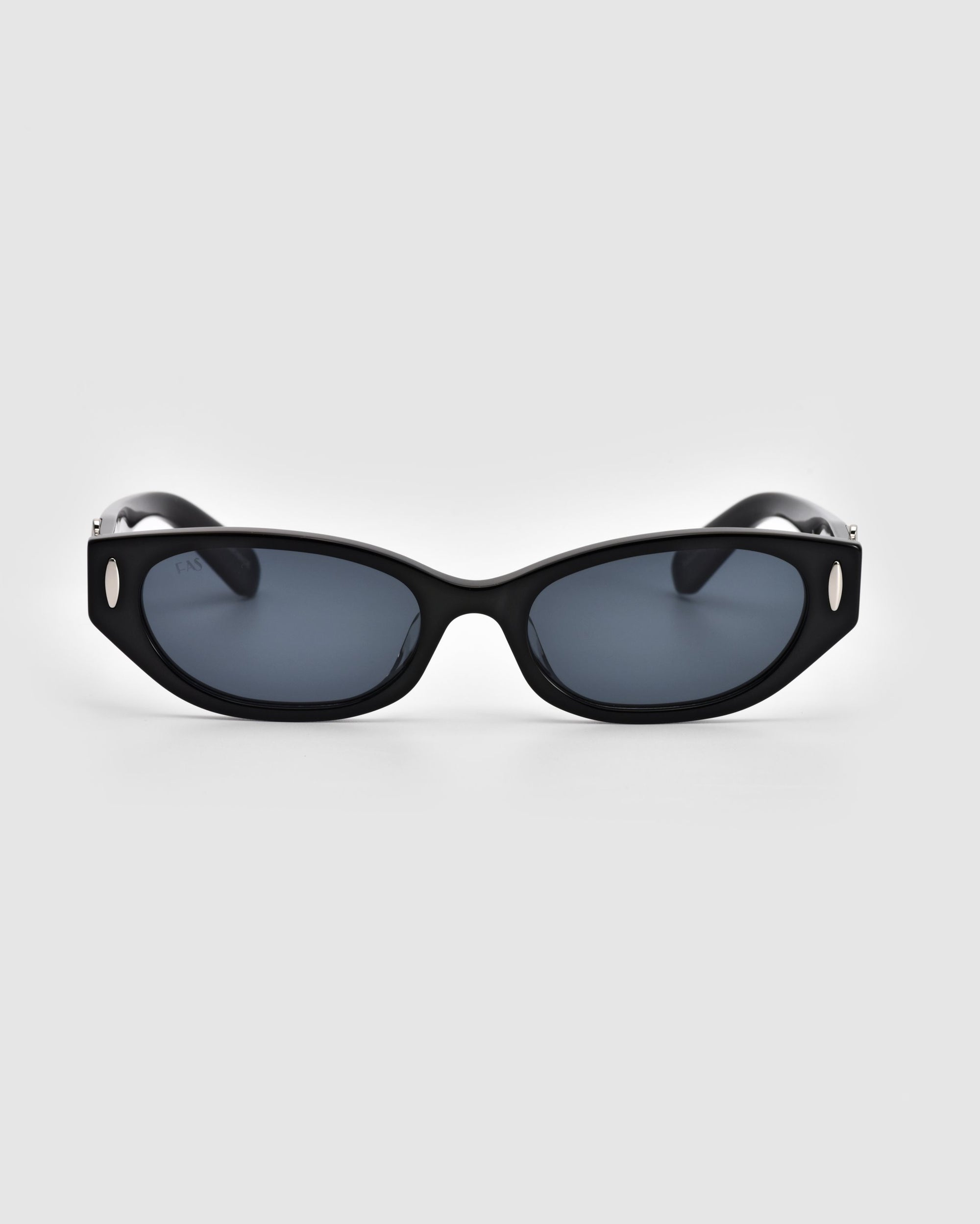 A pair of sleek, black, rectangular Skinny Latte sunglasses by For Art's Sake® featuring dark lenses and small, round silver-toned accents on each corner of the frame. The image displays a front view of these minimalist design sunglasses against a plain, light gray background.