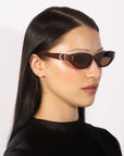 A person with long, sleek, dark hair is wearing small, rectangular Skinny Latte sunglasses by For Art's Sake®, featuring a modern design that channels 90s chic. The individual has a smooth complexion and is dressed in a sleek black top. The photo captures them in side profile against a plain light background.