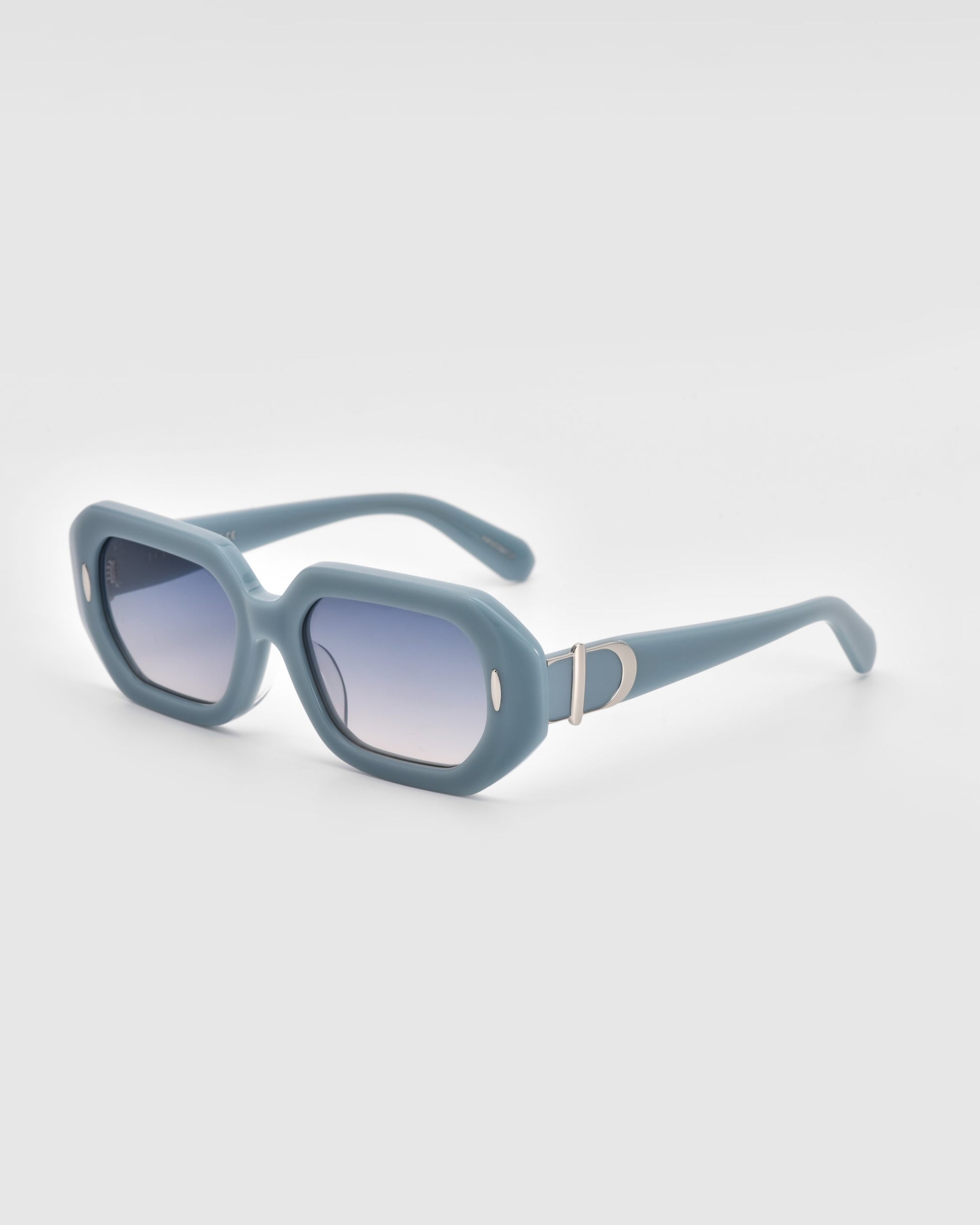 A pair of blue rectangular &quot;Vitamin D&quot; sunglasses by For Art&#39;s Sake® showcasing gradient lenses and an oversized frame. The chunky design includes a silver &quot;D&quot; emblem on each side near the hinges. Crafted from stainless steel and biodegradable acetate, the glasses are displayed against a solid light grey background.