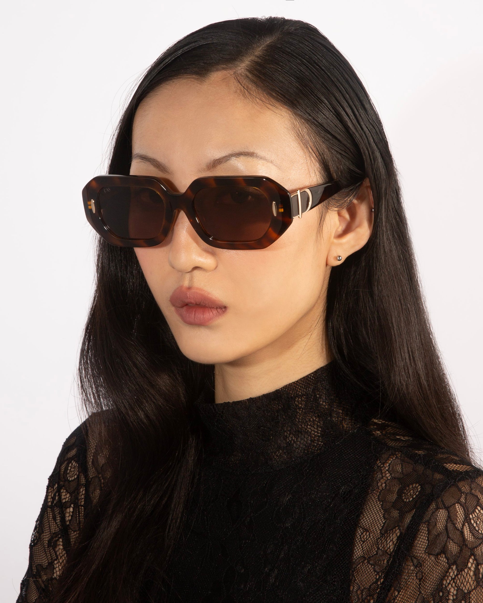 A person with long dark hair is wearing the oversized, rectangular &#39;Vitamin D&#39; black acetate sunglasses by For Art&#39;s Sake®, paired with a black lace top. Their expression is neutral against a plain white background.