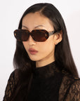 A person with long dark hair is wearing the oversized, rectangular 'Vitamin D' black acetate sunglasses by For Art's Sake®, paired with a black lace top. Their expression is neutral against a plain white background.