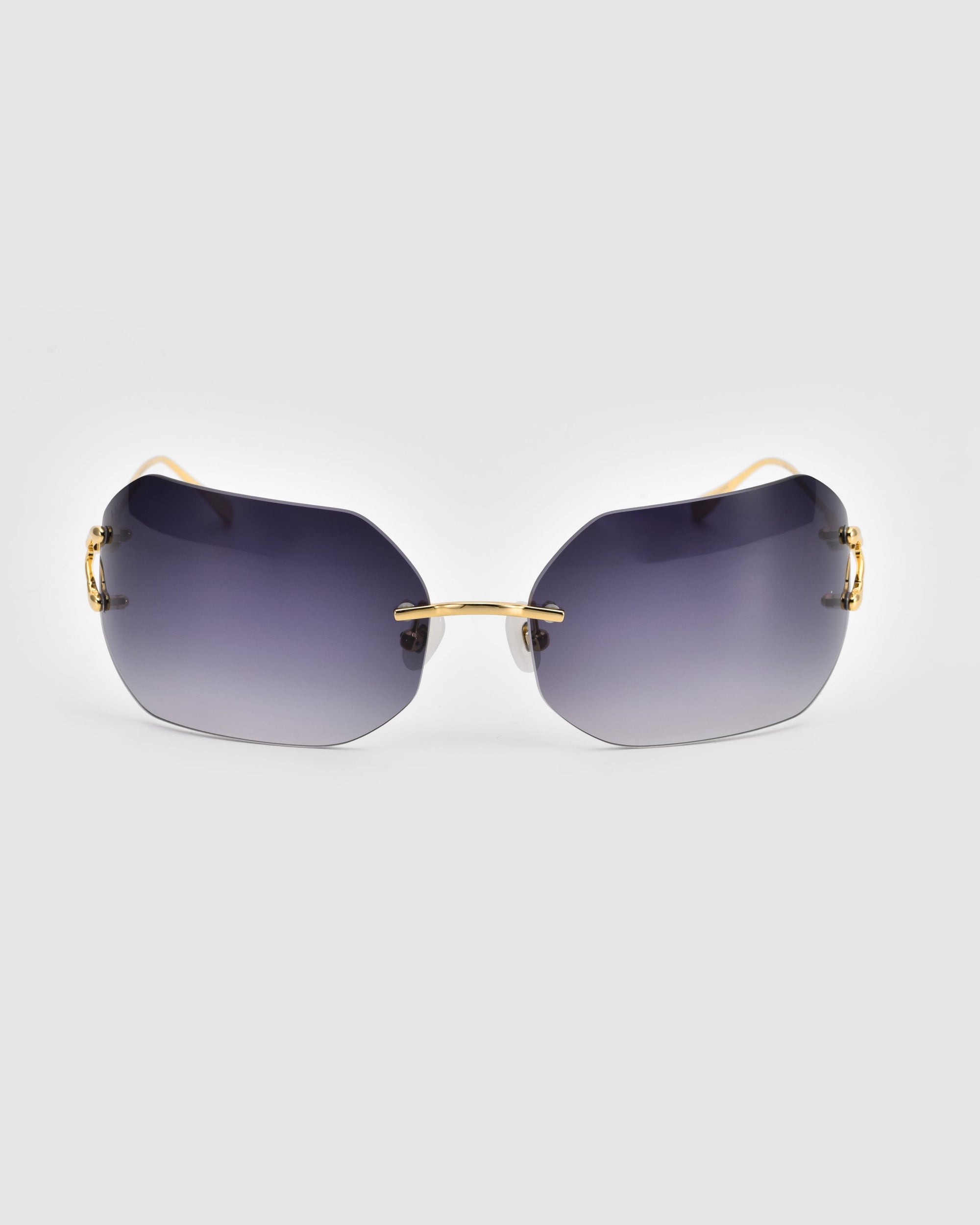 A pair of For Art&#39;s Sake® Hutton sunglasses with dark gradient lenses and thin gold frames, placed on a plain light gray background. The Hutton exudes vintage glamour with its sleek, modern design and slightly curved rectangular lenses.