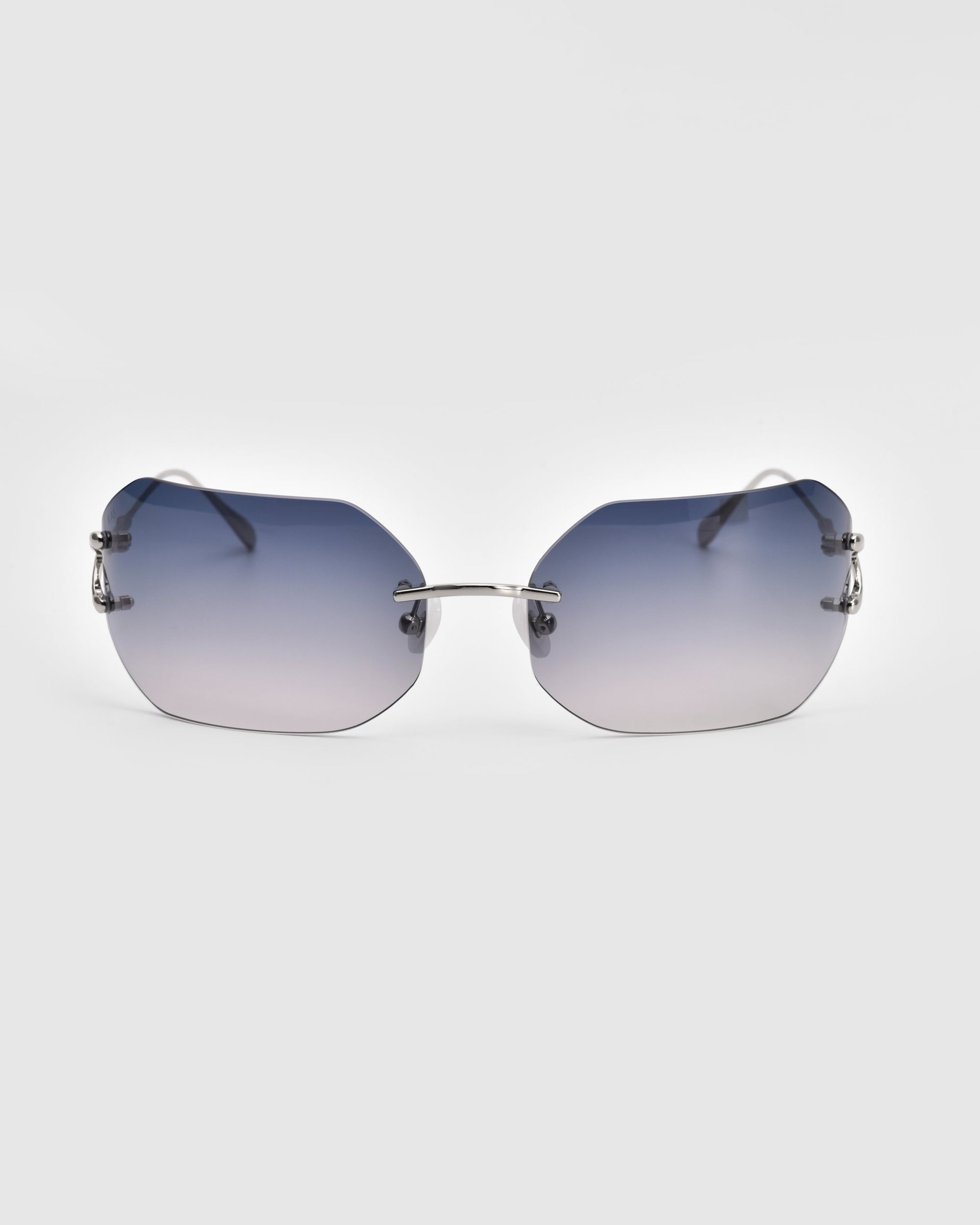 A pair of Hutton sunglasses by For Art's Sake®, featuring gradient blue-tinted rectangular lenses and thin metal arms. The frameless design adds a sleek, modern twist to vintage glamour, set against a clean, white background.