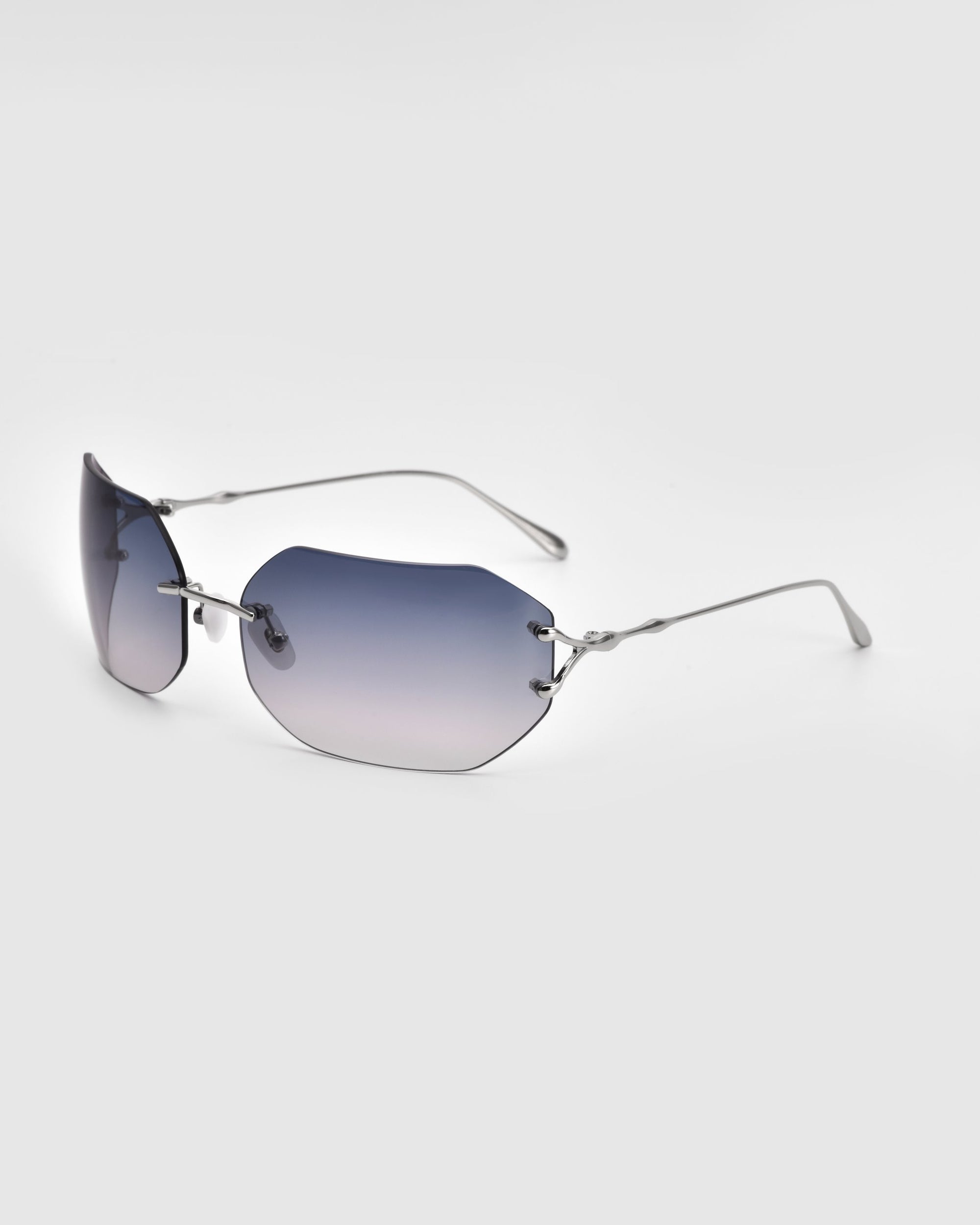 The Hutton sunglasses by For Art's Sake® feature a frameless design and gradient blue-tinted lenses, showcased against a plain white background. These sunglasses exude vintage glamour with their thin, metallic arms featuring a subtle wavy pattern.