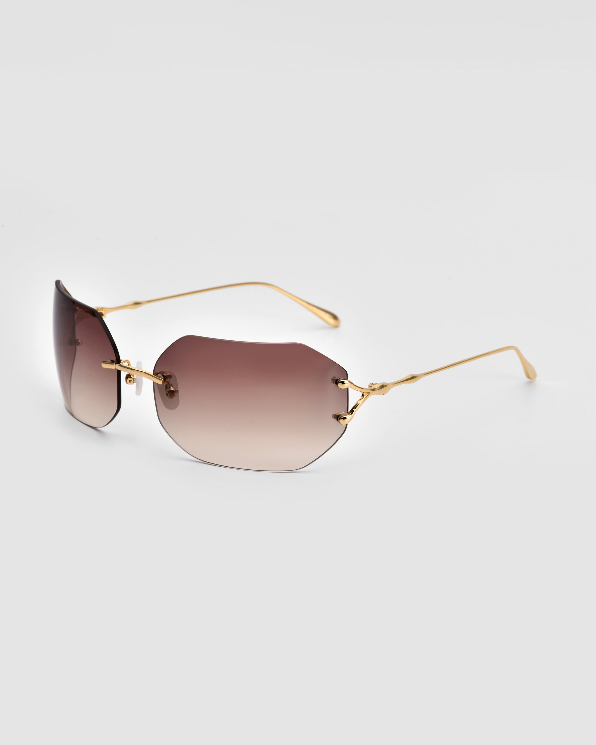 A stylish pair of For Art's Sake® Hutton sunglasses with gradient brown lenses. The sunglasses feature thin, gold-toned metal arms. The frameless design is sleek and modern, exuding vintage glamour with a minimalist appearance.