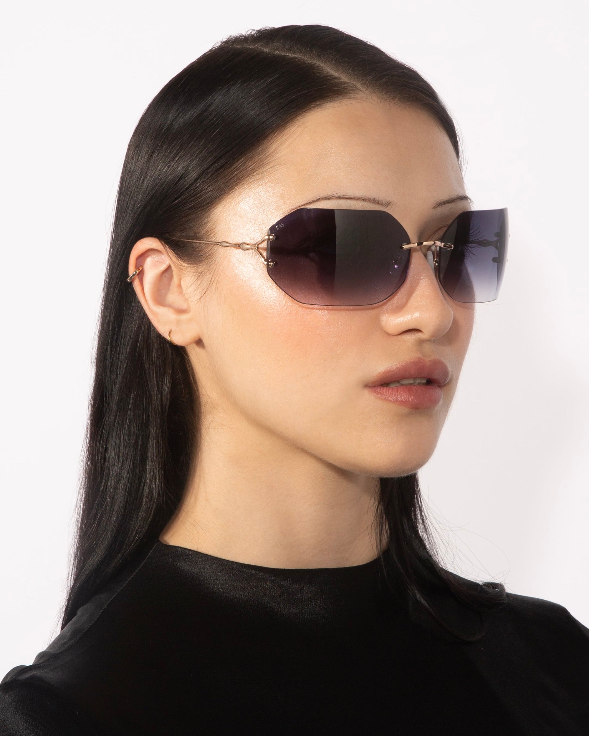 A person with long, straight black hair is wearing oversized Hutton sunglasses by For Art&#39;s Sake®, featuring a thin metal frame and purple-tinted lenses that exude vintage glamour. They are looking to the left against a plain white background, dressed in a black high-neck top.