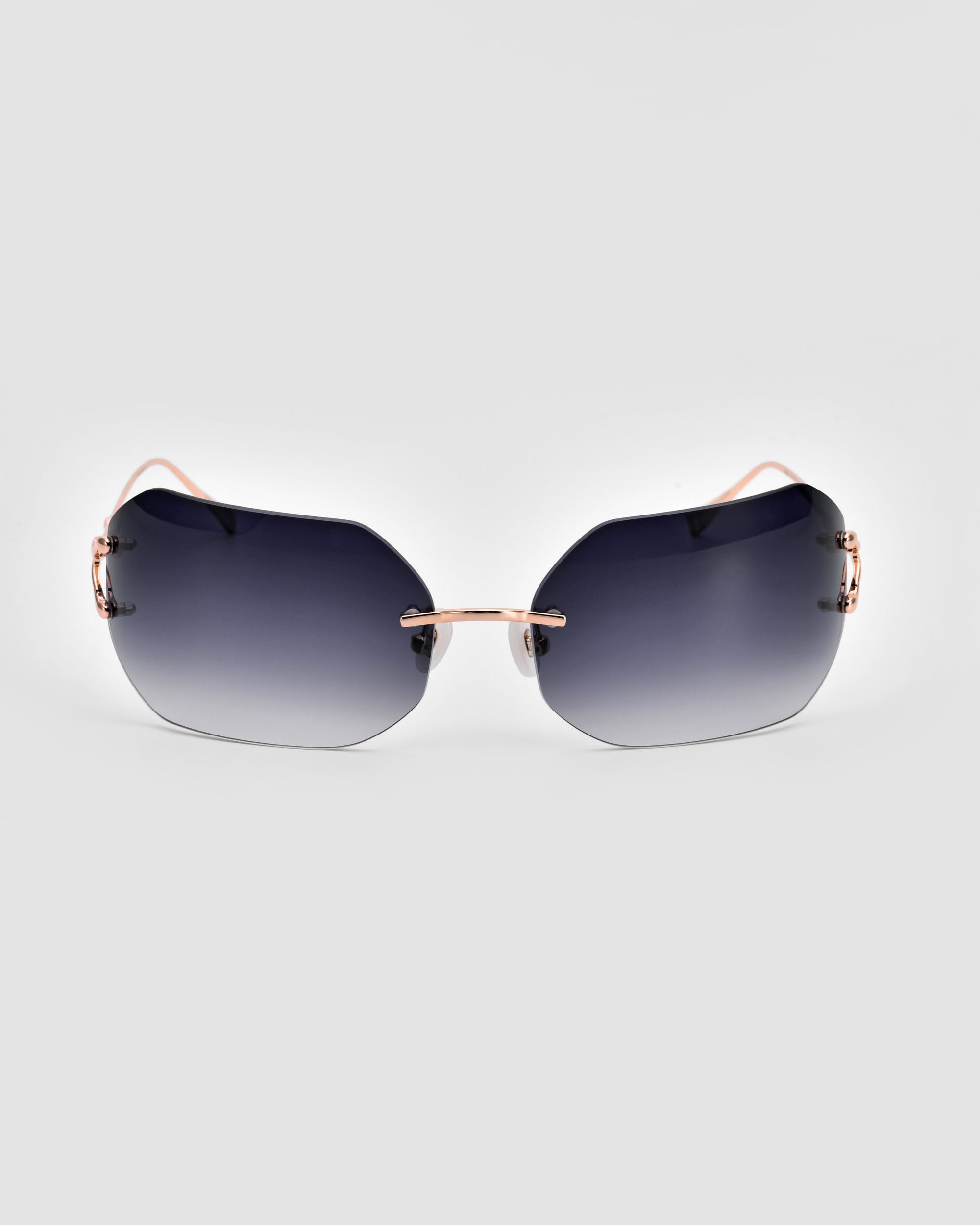 A pair of Hutton sunglasses from For Art&#39;s Sake® embody vintage glamour with their sleek, frameless design, dark gradient lenses, and thin rose gold temples and nose bridge, viewed from the front against a plain white background.