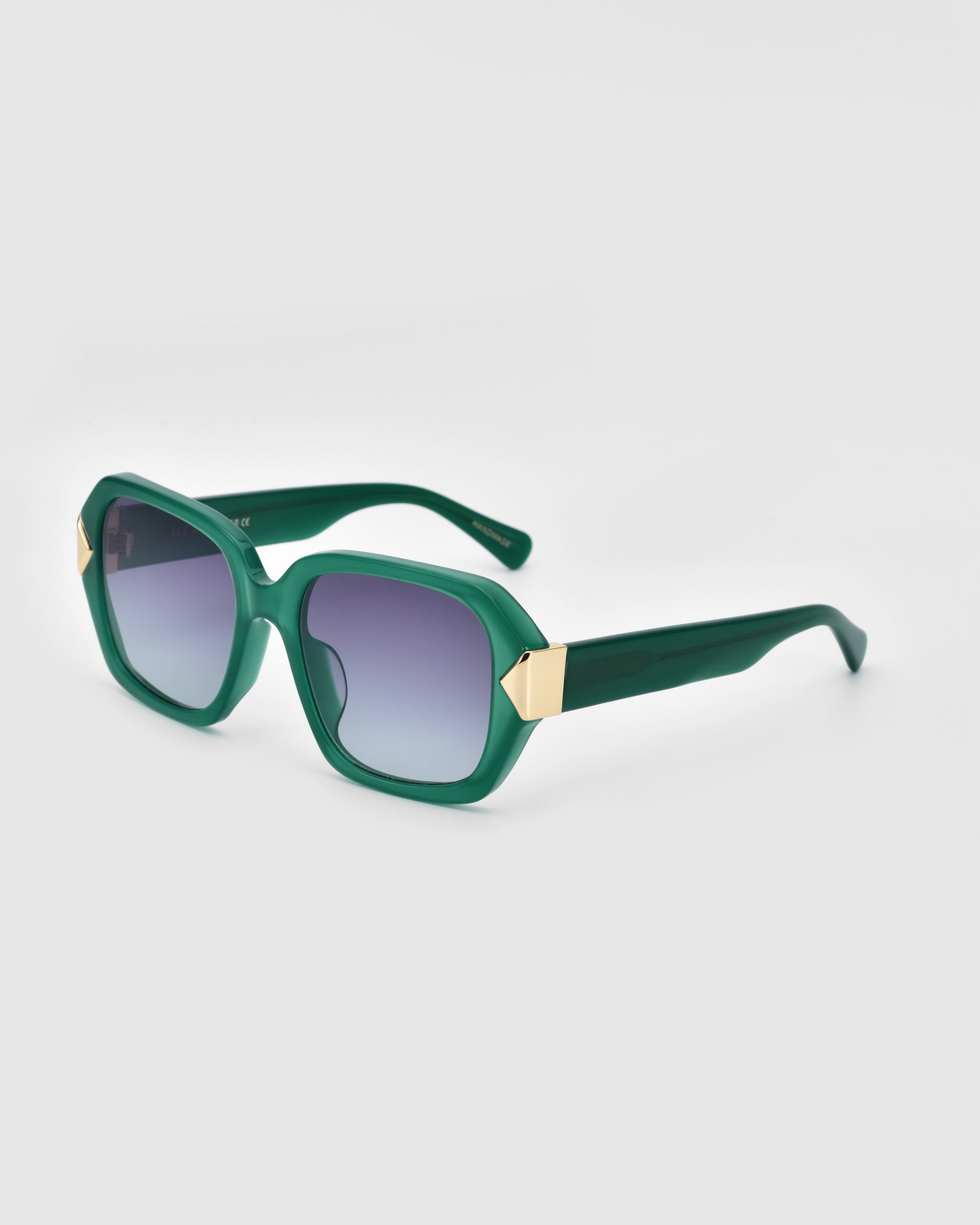 A pair of stylish Frankie oversized sunglasses by For Art&#39;s Sake® with green frames and dark gradient lenses. The temples are also green with golden geometric accents near the lenses, and the overall design boasts a modern, angular shape. The background is plain white.