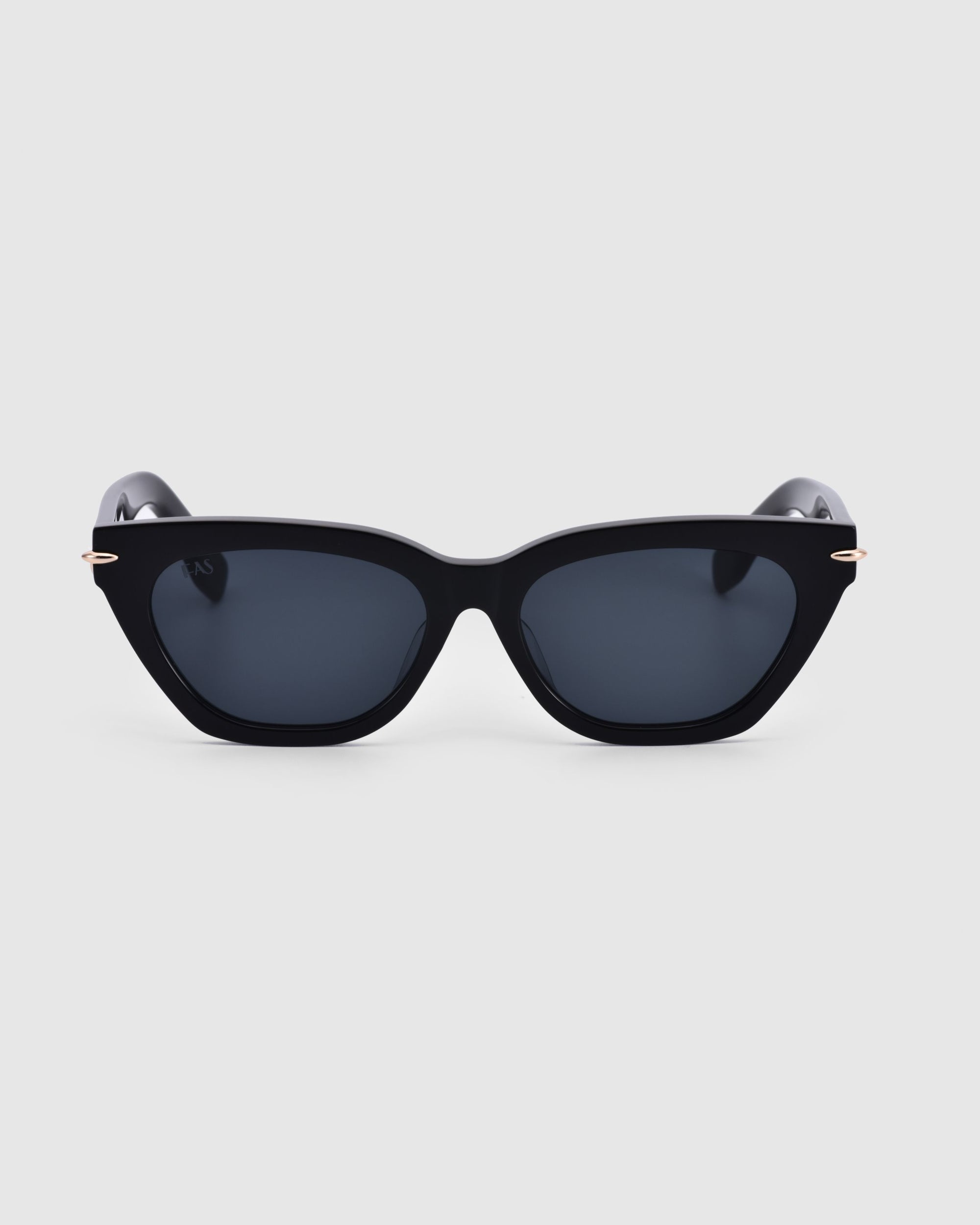 Introducing the Bonbon sunglasses by For Art&#39;s Sake®: a chic pair of black cat-eye silhouette sunglasses with dark tinted lenses. These glossy frames boast a sleek design, highlighted by thin, slightly curved arms. Set against a minimal light grey background to underscore the elegance of the Bonbon model.