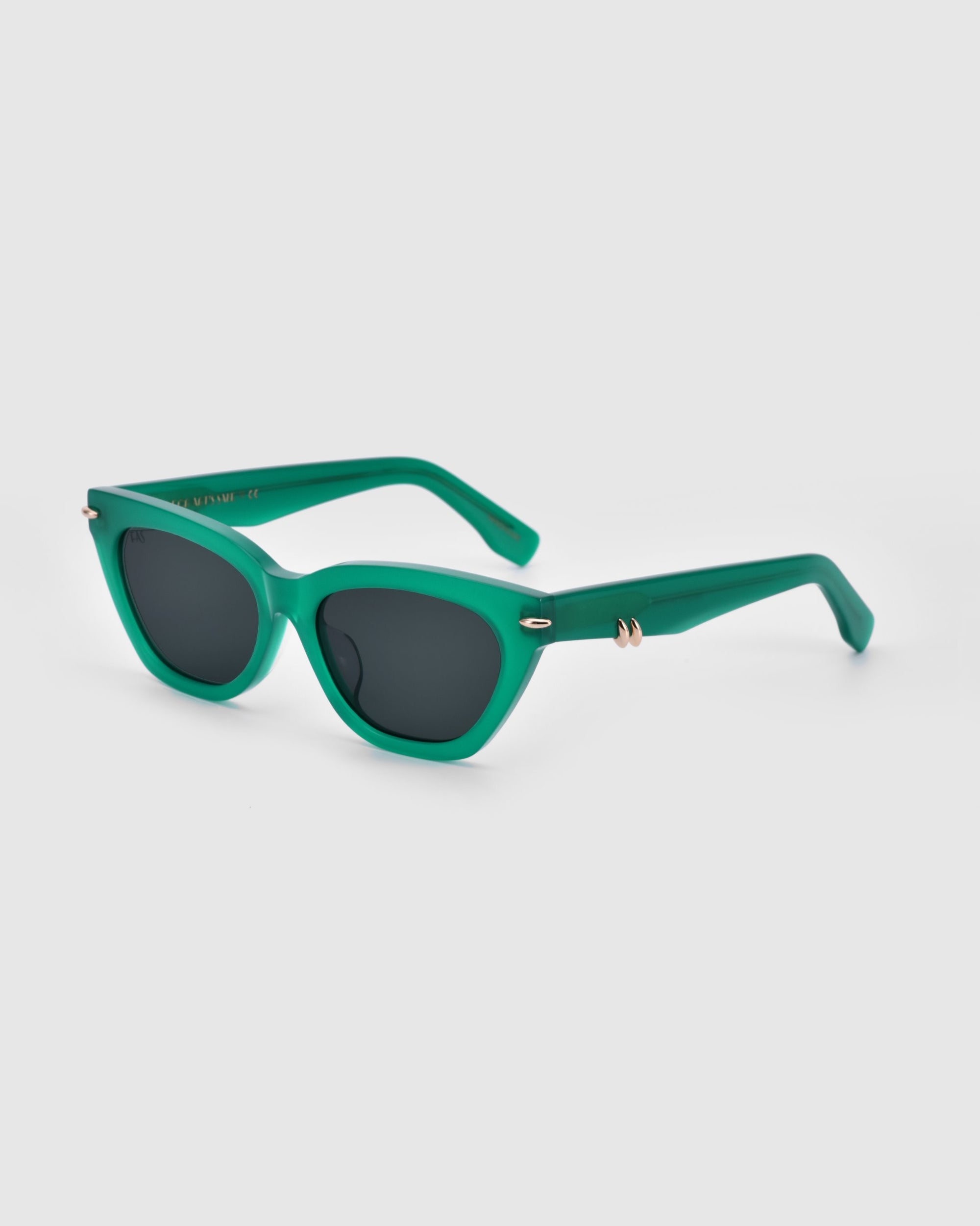 A pair of For Art&#39;s Sake® Bonbon sunglasses in a green, cat-eye silhouette with dark lenses and thick frames, featuring small gold accents near the hinges, set against a plain white background.