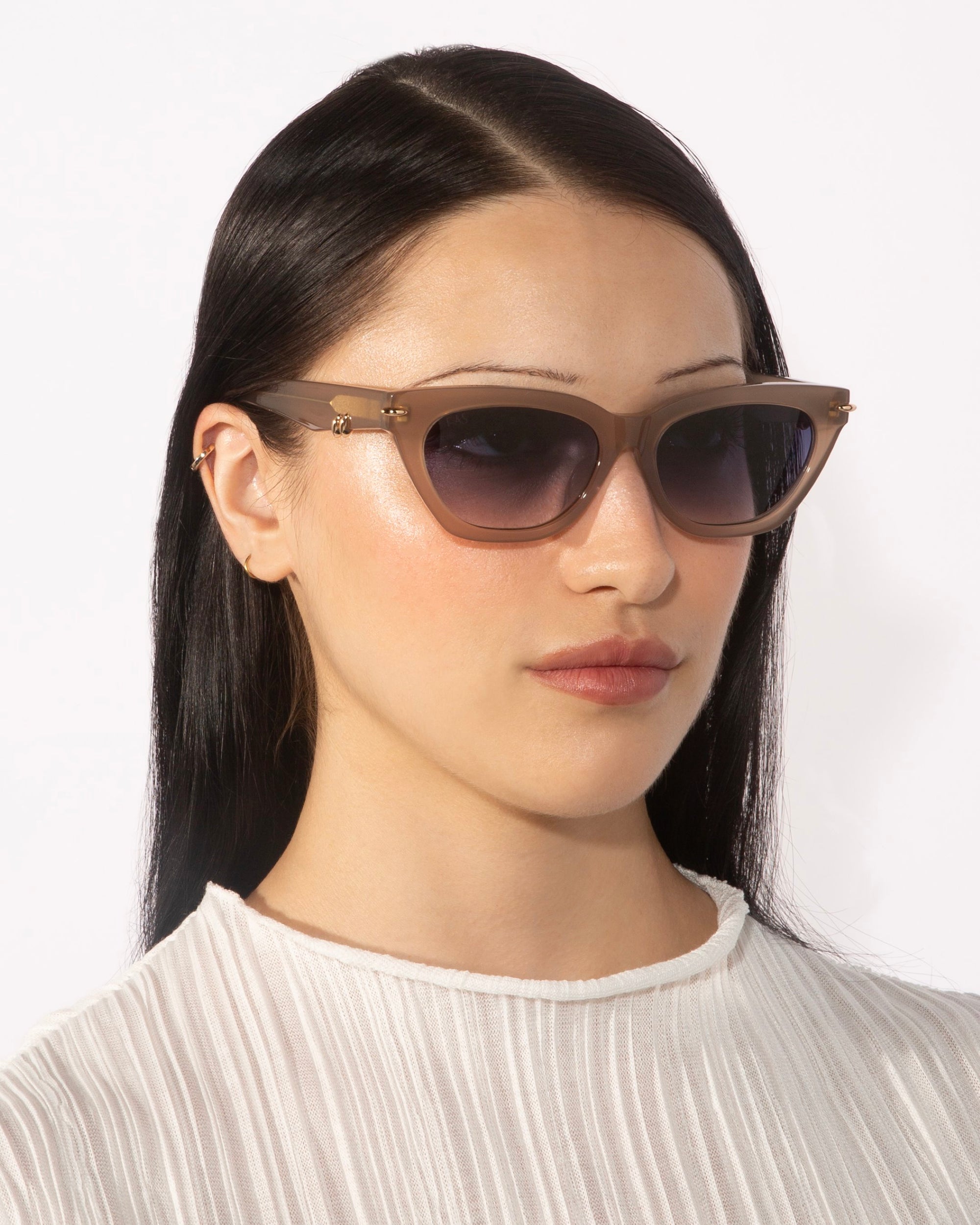 A person with long, straight black hair is wearing a pair of stylish Bonbon sunglasses from For Art&#39;s Sake®, featuring gradient lenses. They are dressed in a light-colored, textured top with a high neckline and are posing against a plain white background.