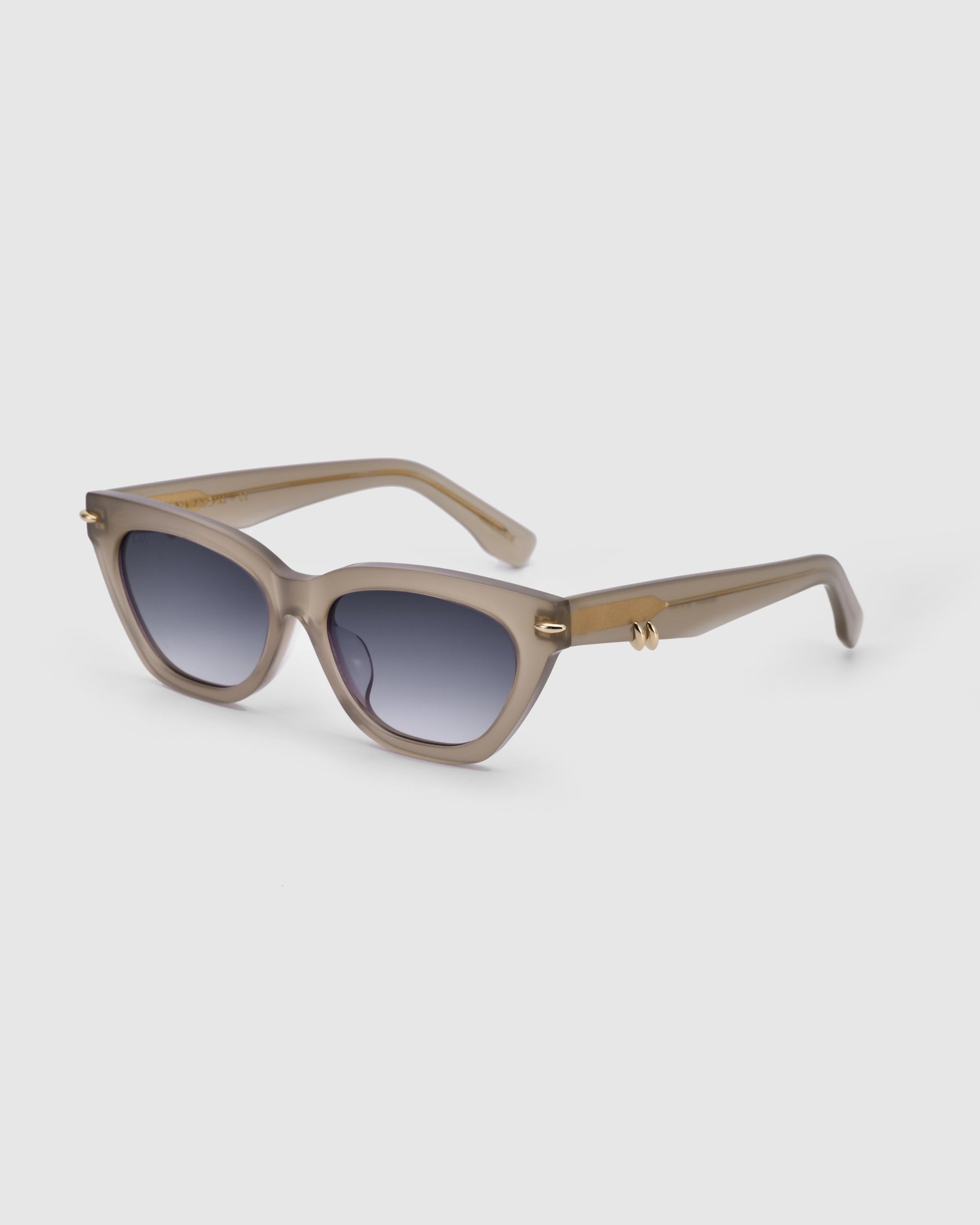 A pair of stylish For Art's Sake® Bonbon sunglasses featuring a taupe-colored frame with gold accents, dark gradient lenses, and an elegant cat-eye silhouette placed on a plain white background. The design is chic and contemporary, offering a blend of fashion and functionality.