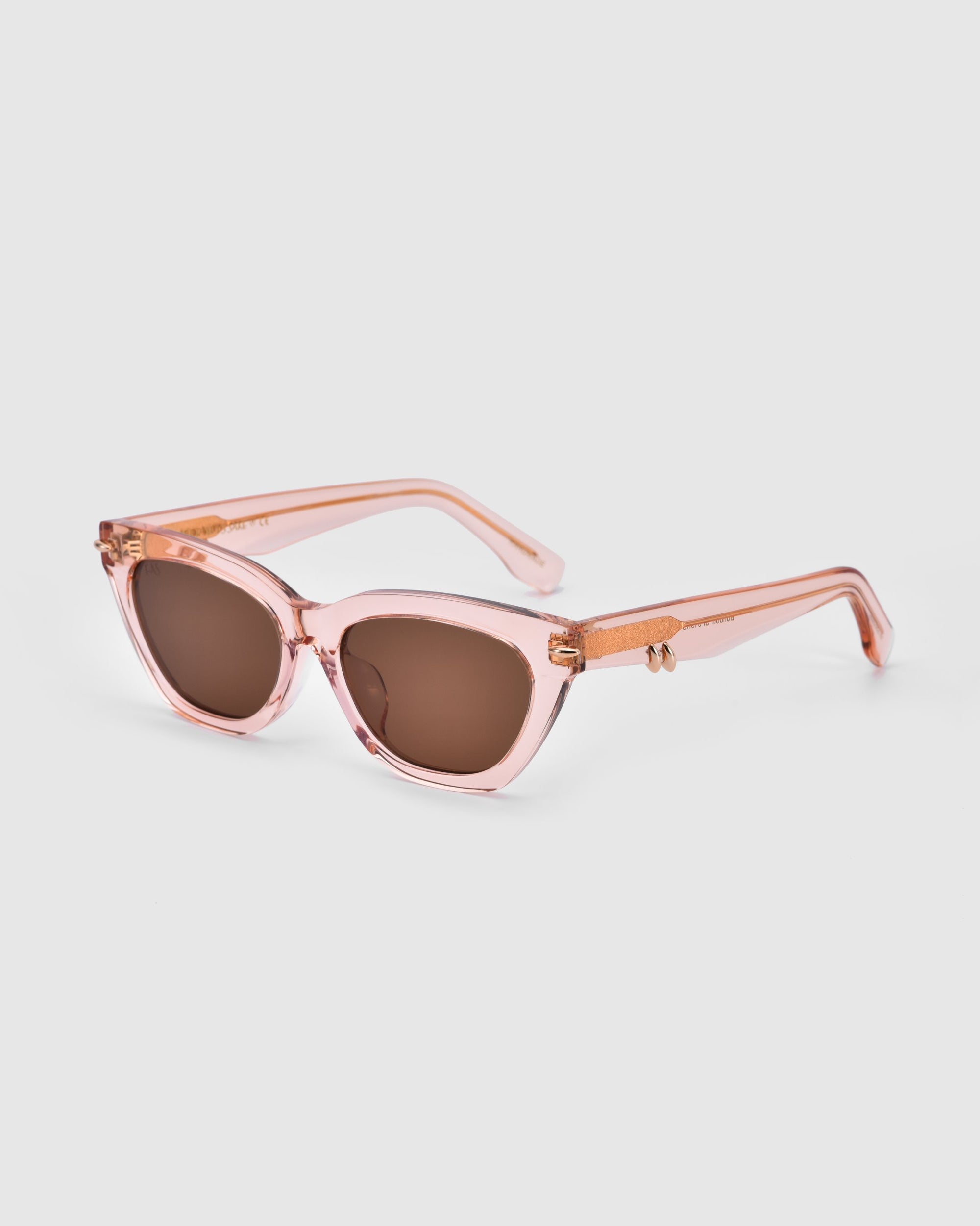 A pair of For Art's Sake® Bonbon sunglasses with dark lenses and thick, transparent pink frames. The arms of the sunglasses feature a matching design with small gold accents on the hinges, adding a touch of flair. The image showcases these chic accessories against a plain white background.
