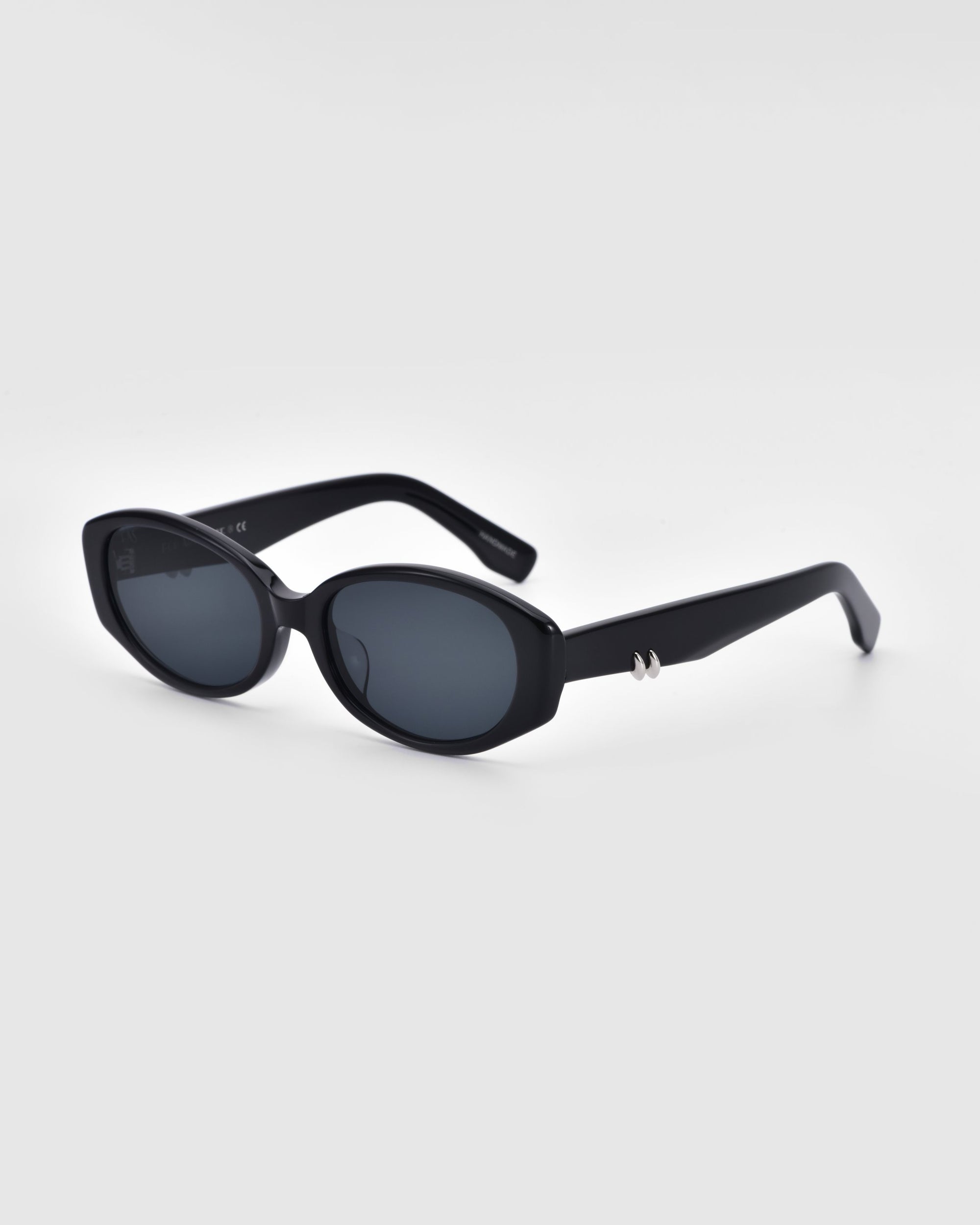 A pair of For Art's Sake® Friday sunglasses with black oval-shaped frames and dark lenses is displayed against a plain white background. These stylish sunglasses feature thick black frames, UV protection, and a small silver embellishment on the temple arms.