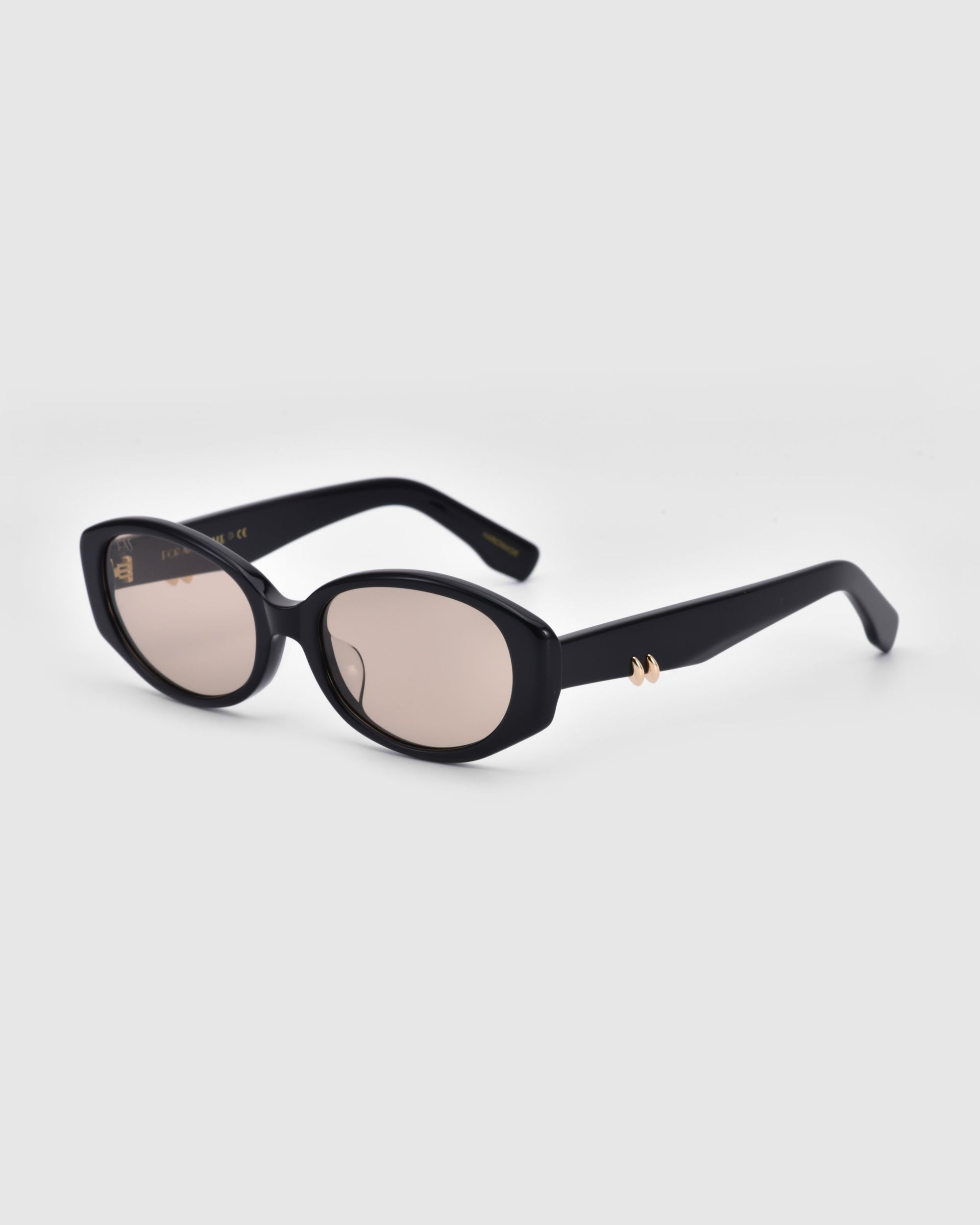 A pair of For Art&#39;s Sake® Friday sunglasses featuring black oval-shaped frames with dark lenses. The slightly curved arms are adorned with a small gold-colored design detail near the hinges, providing both style and UV protection. The background is plain white.