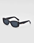 A pair of black Dyer sunglasses from For Art's Sake® with dark lenses is displayed against a plain light gray background. The frames, which offer UV protection, feature small gold accents at the corners near the lenses and on the temples.