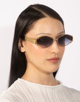 A person with long, straight black hair is wearing angular Empress sunglasses by For Art's Sake® with dark lenses and a white textured top. The oversized frame enhances the elegance of the luxury eyewear against a plain white background.