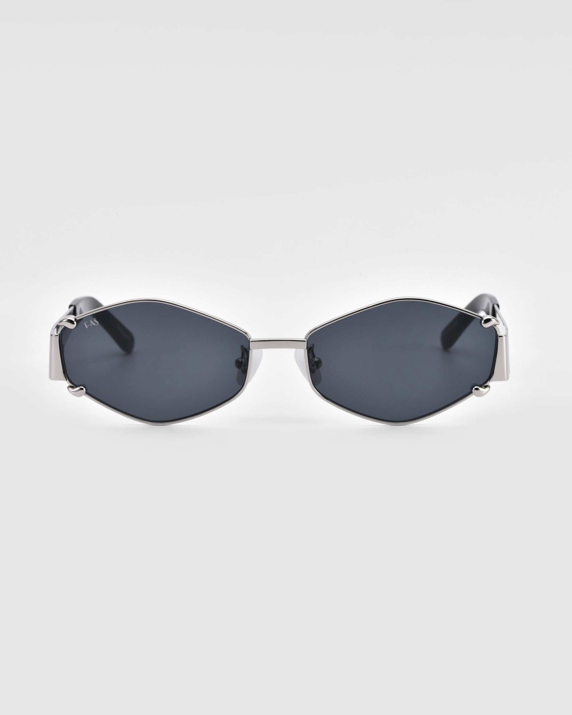 A pair of luxury, geometric Empress sunglasses by For Art&#39;s Sake®, featuring hexagonal dark lenses and a metallic frame, is centered against a plain white background. The modern and stylish design boasts sleek lines and minimalistic detailing, offering premium UV protection for discerning tastes.