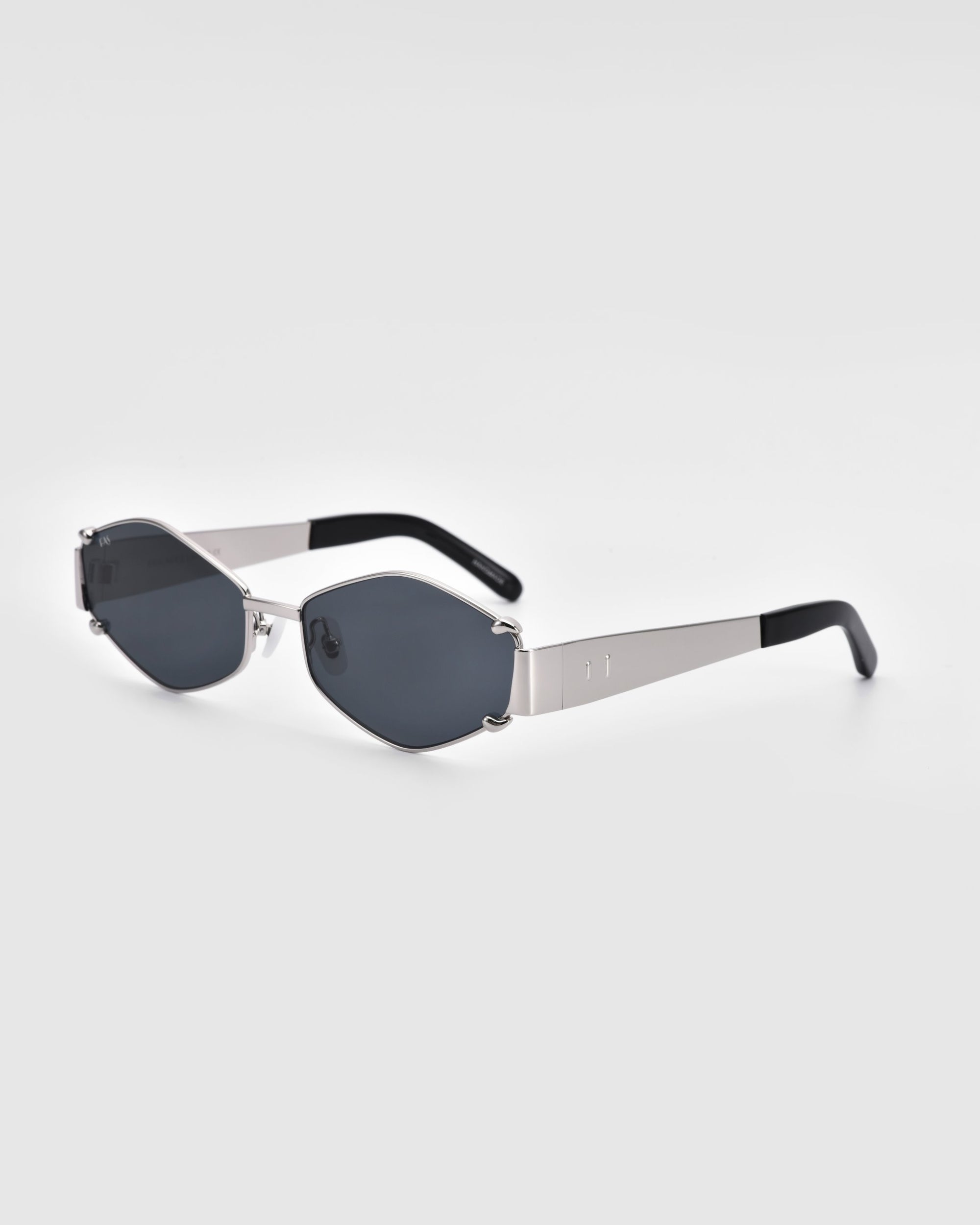 A pair of For Art's Sake® Empress hexagonal luxury sunglasses with dark tinted lenses and silver metal frames. The arms, black at the tips, add a sleek contrast to the overall design. These UV protection sunglasses are set against a plain white background, emphasizing their stylish and functional appeal.