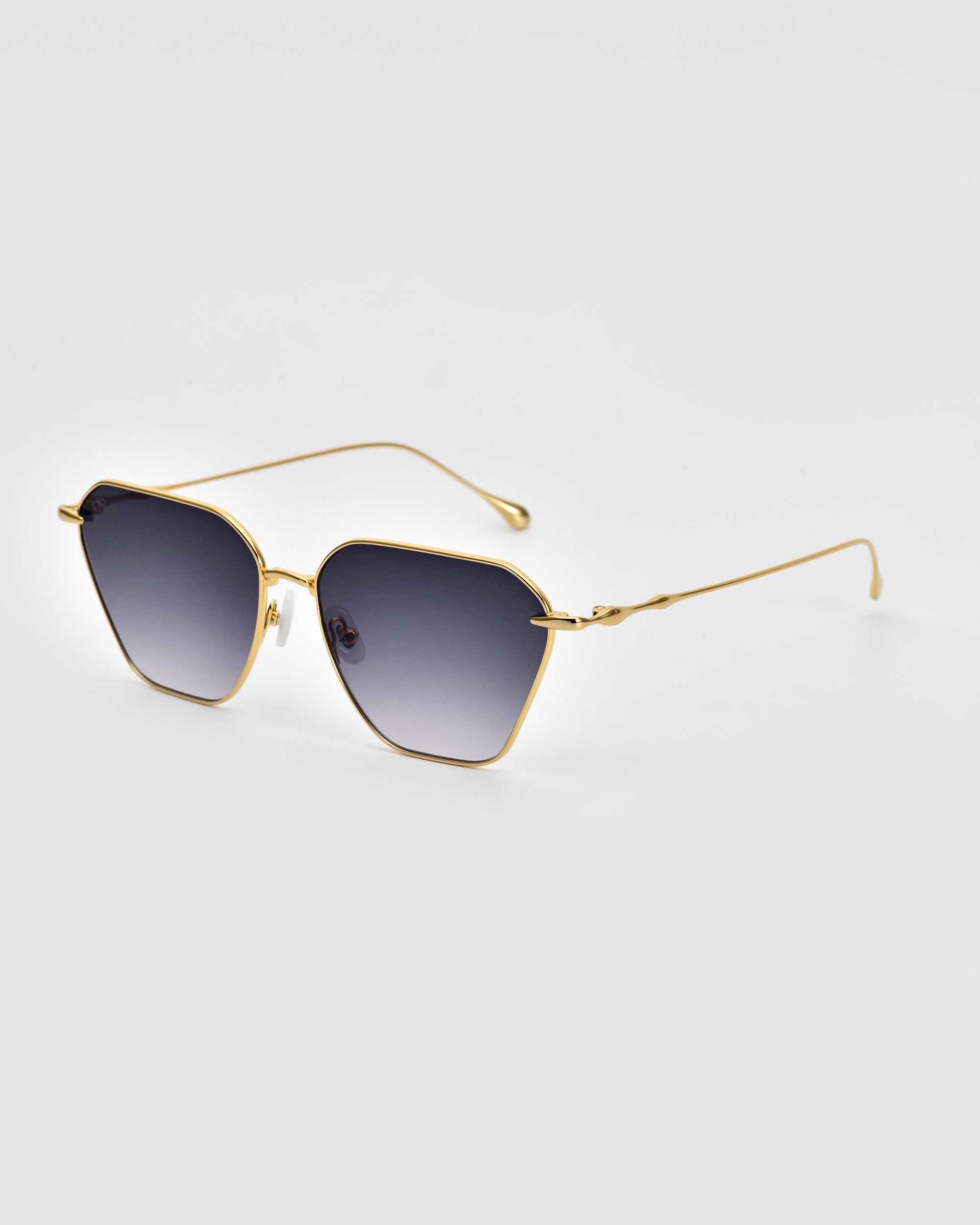 A pair of stylish Cece Sunglasses by For Art&#39;s Sake® featuring gold metal frames and dark gradient lenses. Set against a plain white background, the lenses boast a subtle hexagonal geometric shape, while the thin metal arms curve slightly at the tips.