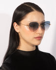 A woman with long, straight black hair wears stylish For Art's Sake® Fifi sunglasses with a gradient tint. She is dressed in a black top and is shot against a plain white background. Her chic look is completed with an 18k gold-plated ear cuff on her left ear.