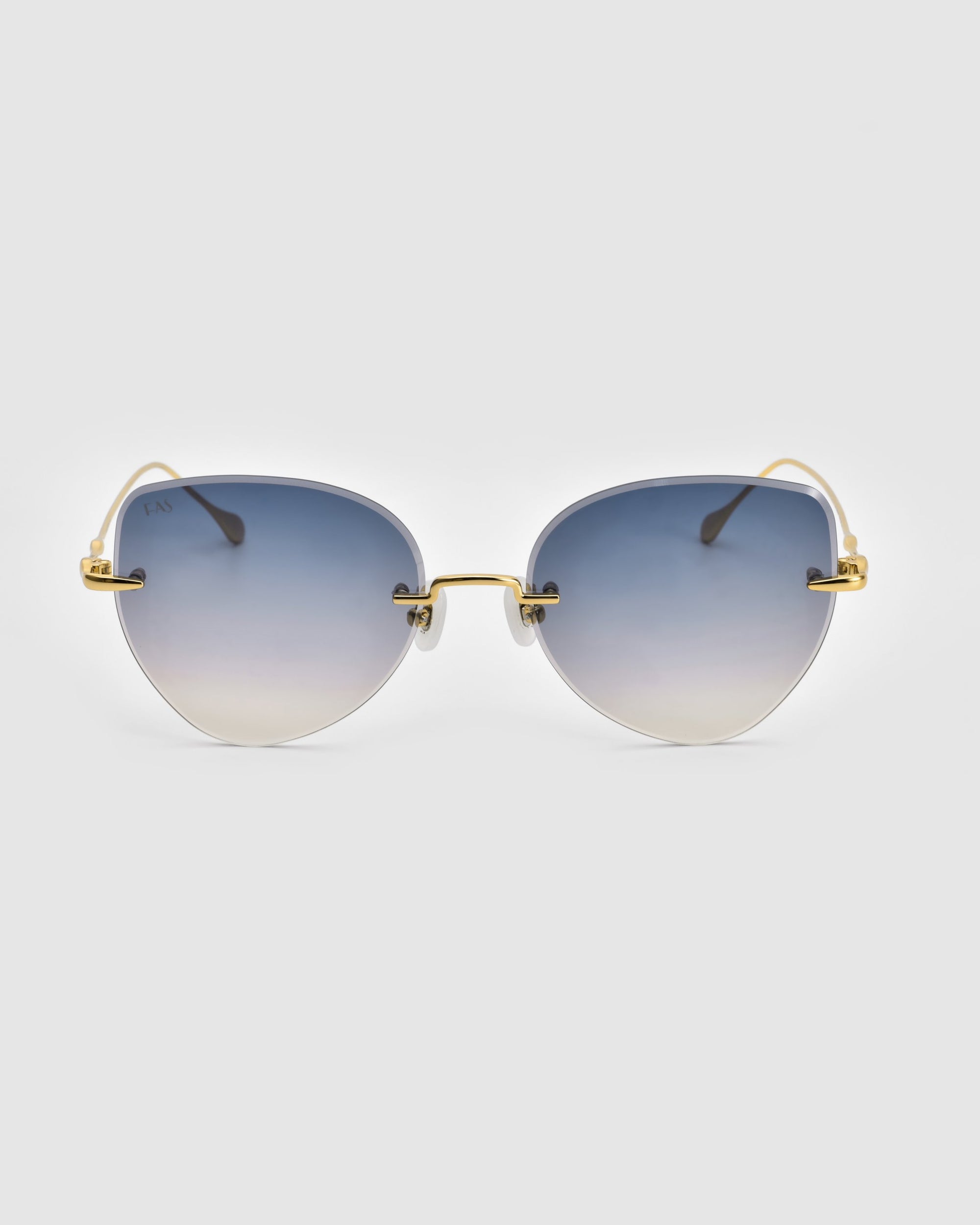 A pair of Fifi sunglasses from For Art&#39;s Sake® boasts gradient blue lenses and 18k gold plating on the wireframe temples. The minimalistic, modern design showcases a cat-eye frameless silhouette, delivering a sleek and fashionable appearance against a white background.