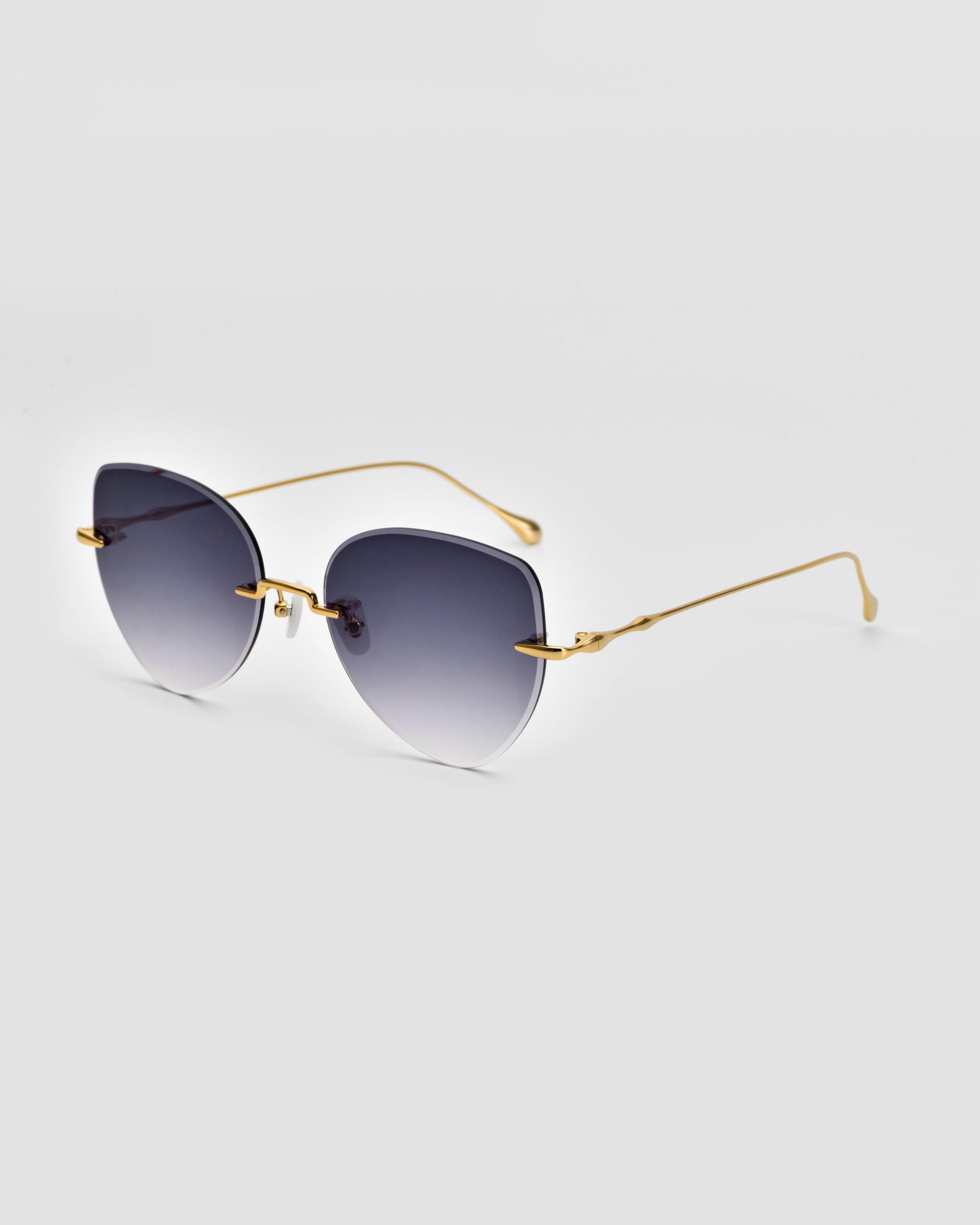 A pair of stylish For Art's Sake® Fifi Sunglasses featuring gradient black lenses and 18k gold-plated metal frames. The cat-eye frameless silhouette highlights the sleek design, complemented by thin gold arms and minimalistic end tips. The background is plain white.