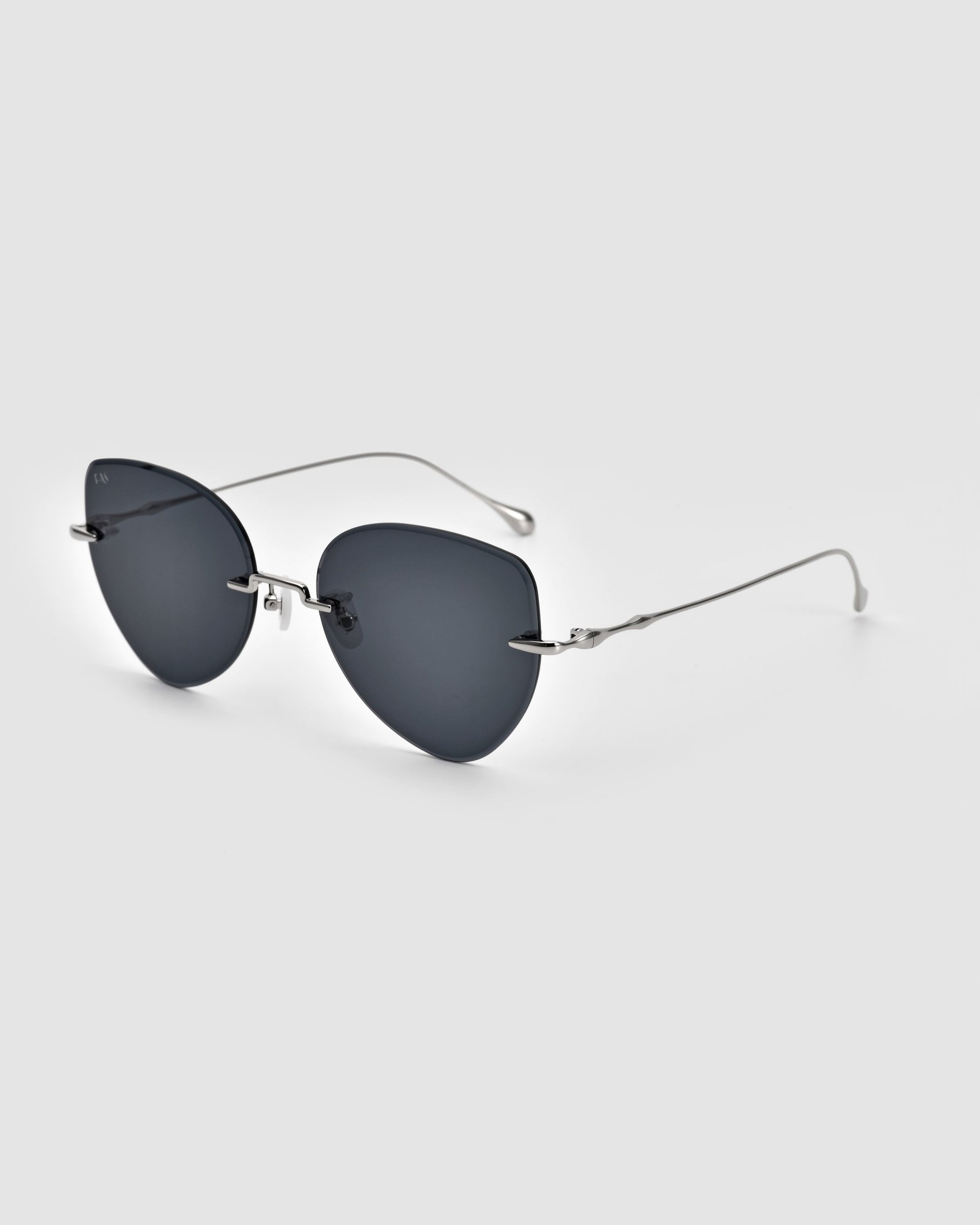 The Fifi Sunglasses from For Art&#39;s Sake® are a pair of stylish, frameless sunglasses showcasing dark, rounded lenses and thin, silver metal arms. They feature a minimalist design with a sleek nose bridge and silicone nose pads, all set against a neutral gray background. The elegant gradient lenses add an extra touch of sophistication.