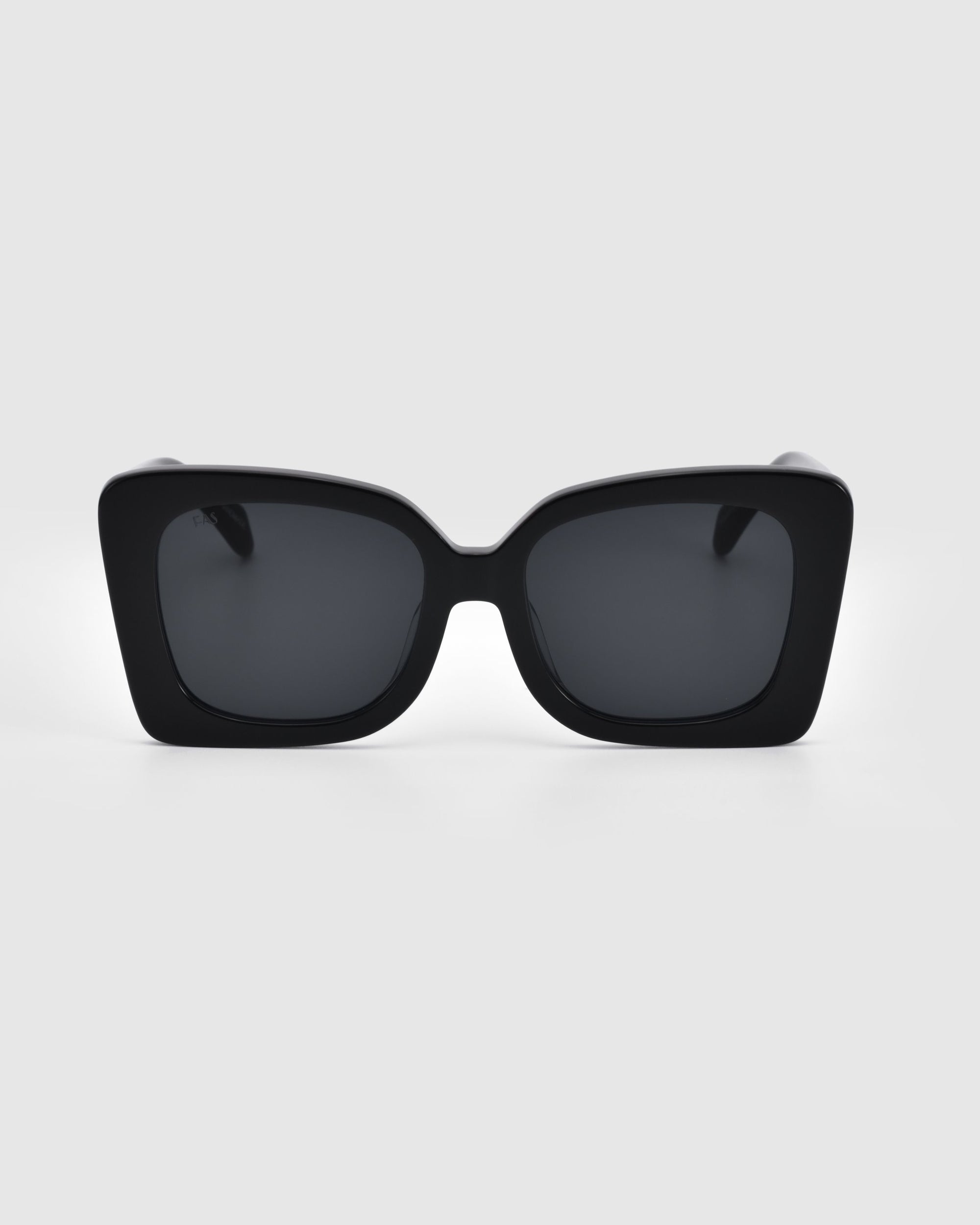 A pair of Ribbon Sunglasses from For Art's Sake® featuring thick, glossy black rectangular frames and dark lenses is centered against a white background. This stylish accessory is perfect for any occasion.