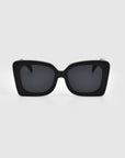 A pair of Ribbon Sunglasses from For Art's Sake® featuring thick, glossy black rectangular frames and dark lenses is centered against a white background. This stylish accessory is perfect for any occasion.