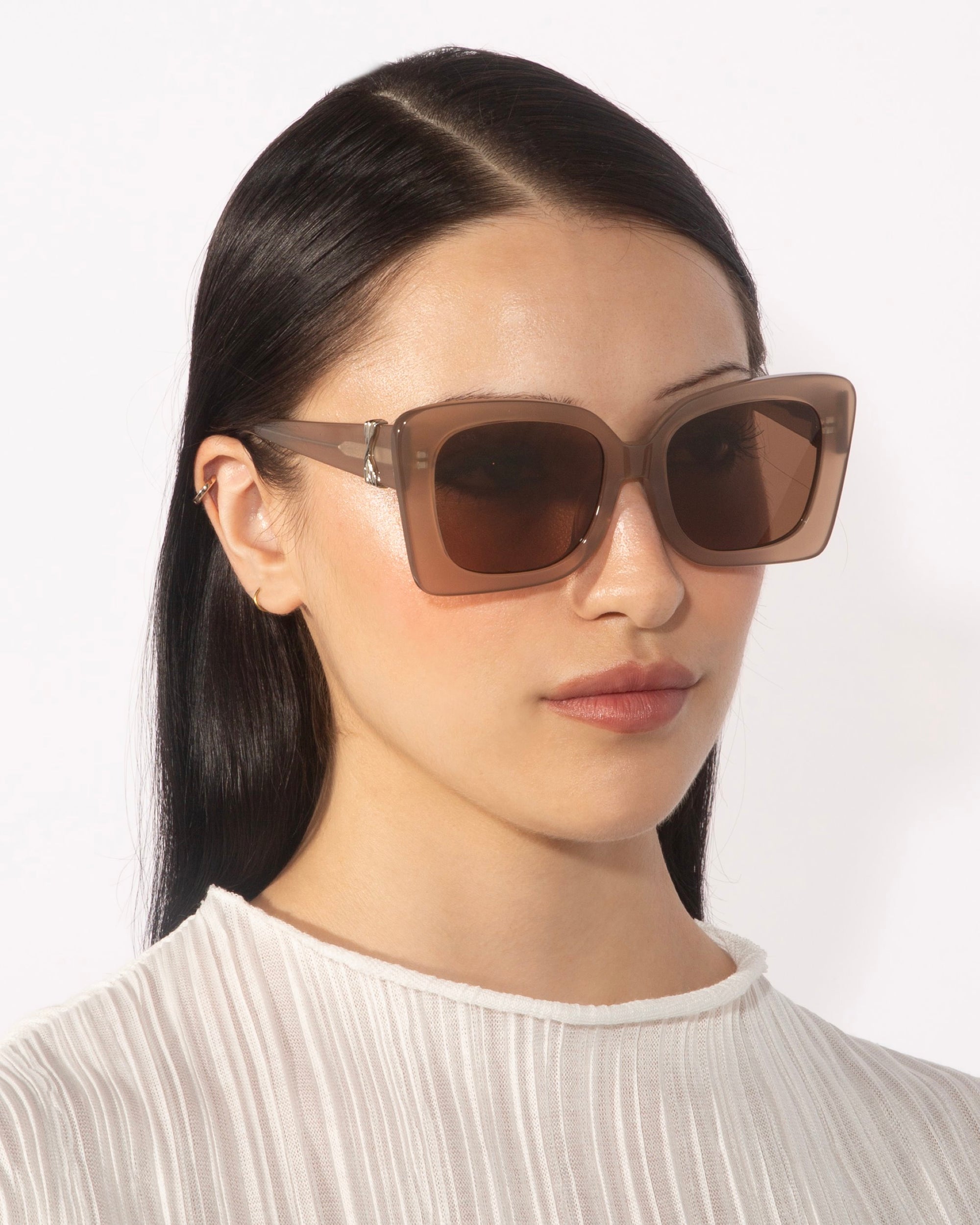 A person wearing the For Art&#39;s Sake® Ribbon oversized square brown sunglasses and a white textured top. They have straight, long, dark hair and a neutral expression, facing slightly to the left against a plain white background.