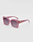 A pair of stylish For Art's Sake® Ribbon Sunglasses with oversized, square-shaped frames in a pink hue. The sunglasses feature dark tinted lenses and gold accents on the arms near the hinges. These sustainable sunglasses are set against a plain white background.