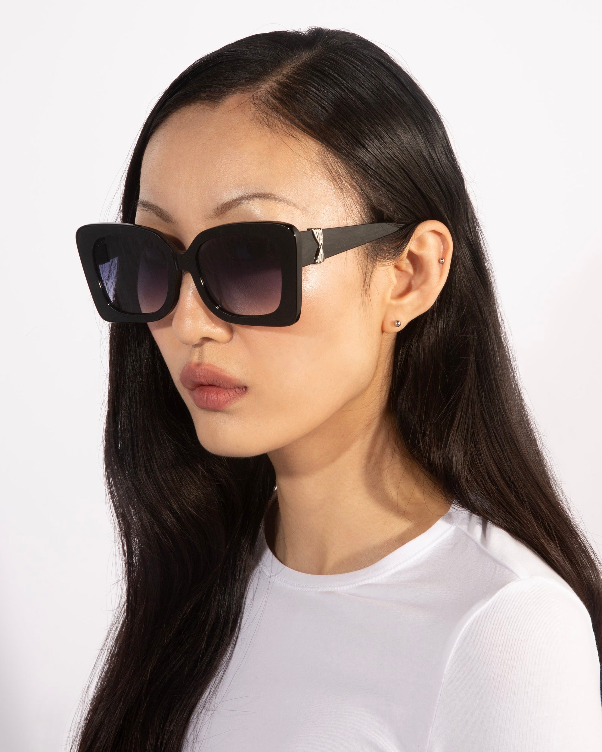 A person with long, straight black hair is wearing the Ribbon oversized, square black sunglasses from For Art's Sake®—a stylish accessory—and a white top. Their expression is neutral, and they are set against a plain white background.