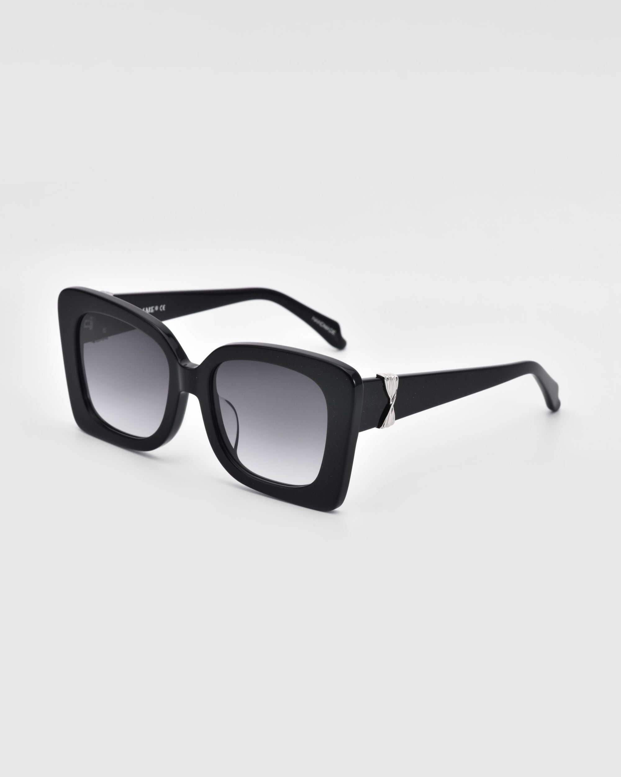 A pair of black square-framed Ribbon Sunglasses from For Art&#39;s Sake®, featuring dark tinted lenses and silver hinge accents. The stylish accessory is positioned at an angle, showcasing both the front and side design, against a plain white background.