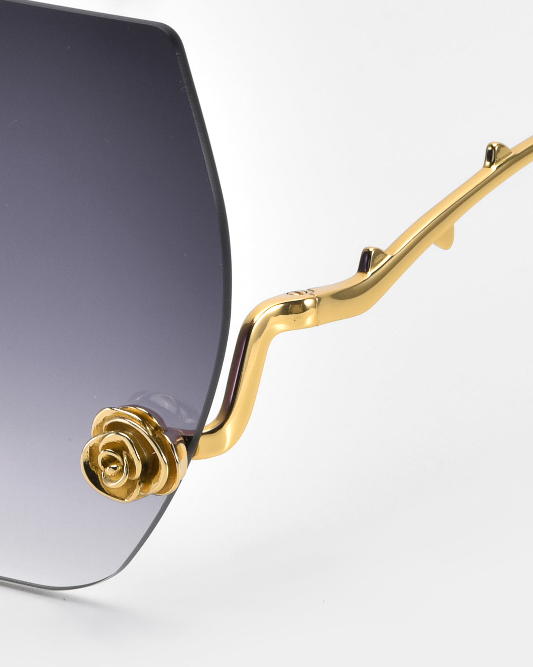 Close-up of La Vie En Rose sunglasses by For Art's Sake®. The gold frame intricately mimics a rose stem with sculpted rose ornaments on the arms, and gradient lenses transition elegantly from dark to light.