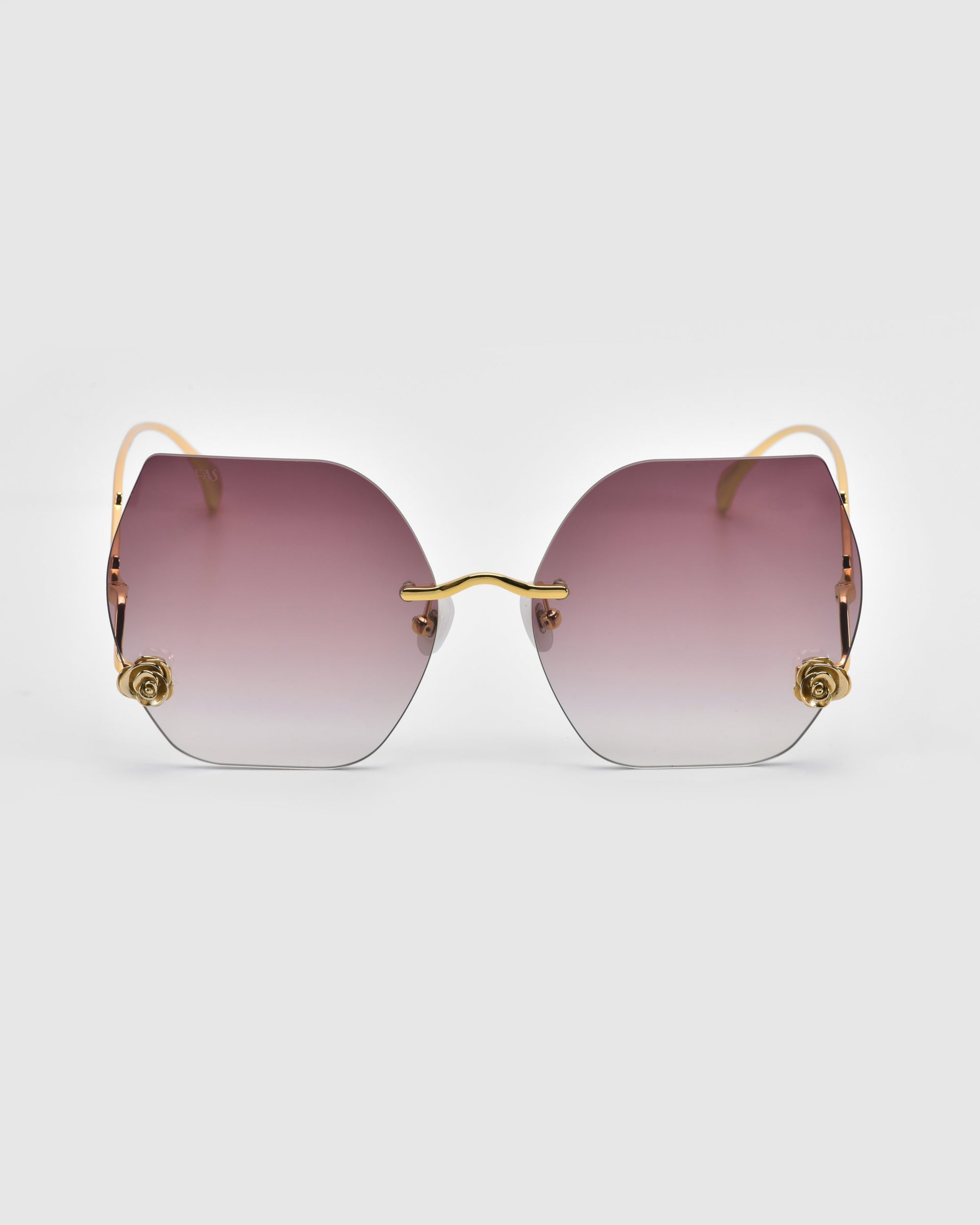 Explore For Art's Sake®'s La Vie En Rose Collection, showcasing chic sunglasses with gradient pink to clear octagonal lenses. These elegant shades feature thin gold frames and ornate temple embellishments, set against a plain white background.