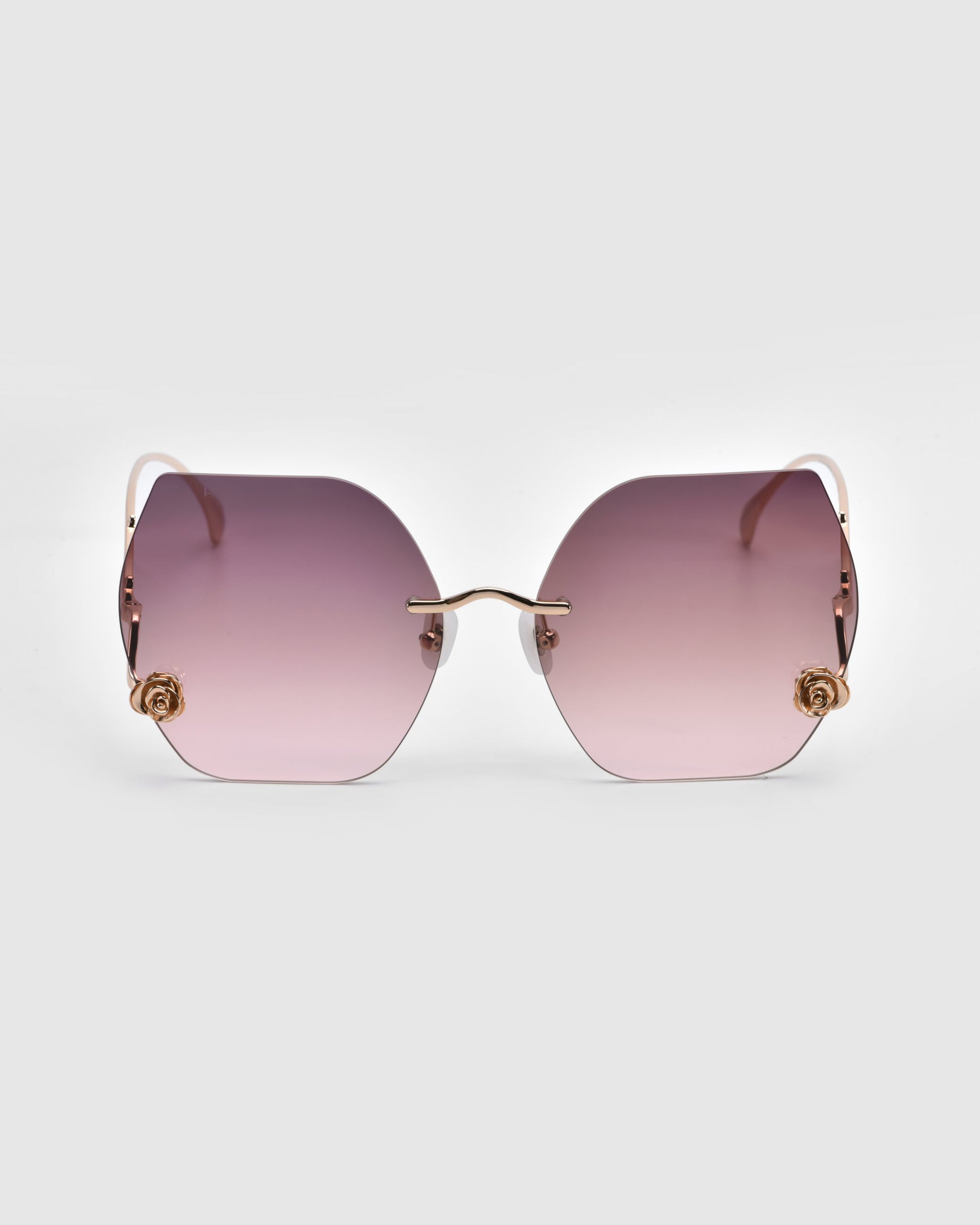 From the Rose Garden Collection, the "La Vie En Rose" sunglasses by For Art's Sake® showcase oversized frameless gradient pink lenses with gold rose ornaments at each corner, complemented by a gold nose bridge and temples against a light gray backdrop.