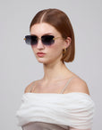 A short-haired woman is styled in gradient oversized frameless lenses from For Art's Sake® Rose Garden Collection and gold hoop earrings, wearing an off-shoulder white top, posing against a plain background.