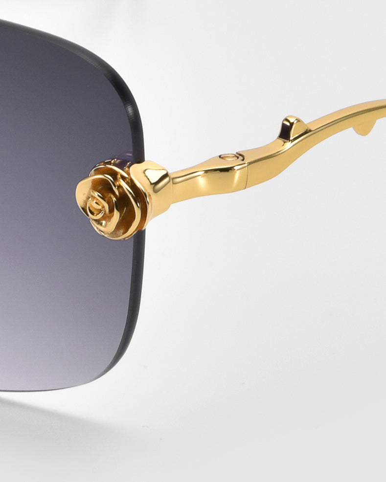 Close-up of the Rose Garden sunglasses by For Art's Sake®, featuring gold-colored arms with sculpted rose ornaments. The dark lenses create a sophisticated and elegant look.